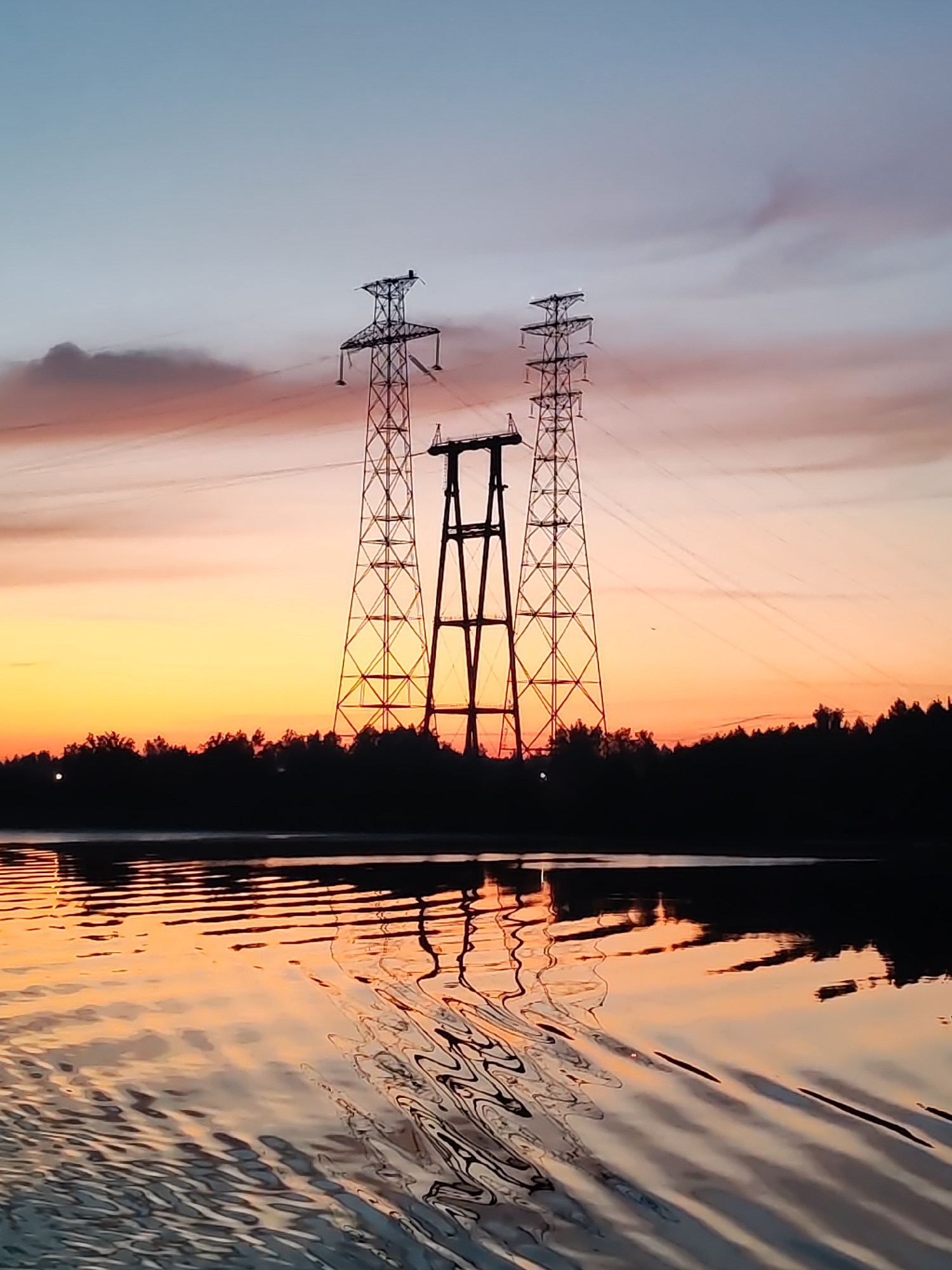 Sunset illuminates power pylons along Konakovo river at dusk