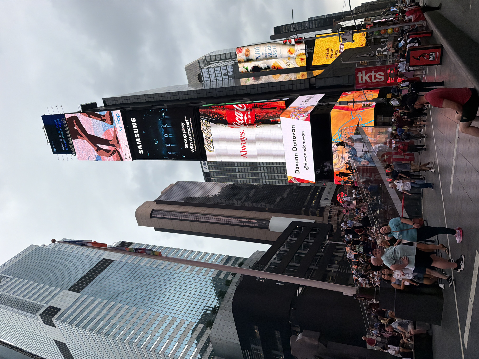Evening traffic flows through Times Square under cloudy skies