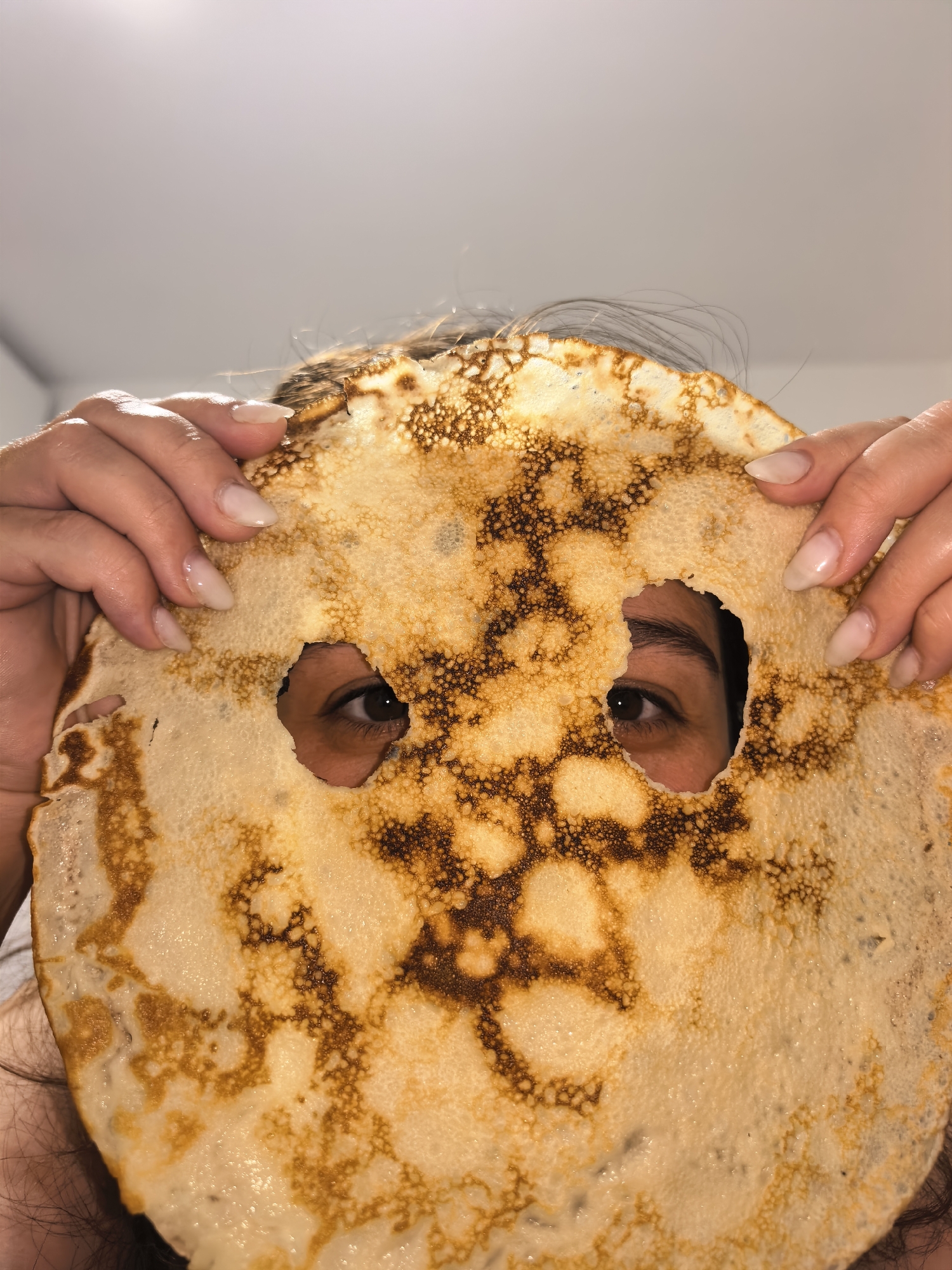 Person makes crepes, plays with pancake mask at unknown location