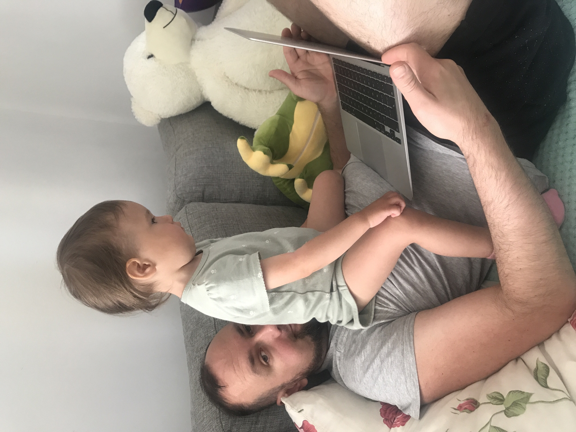 Father and baby share laptop time on sofa