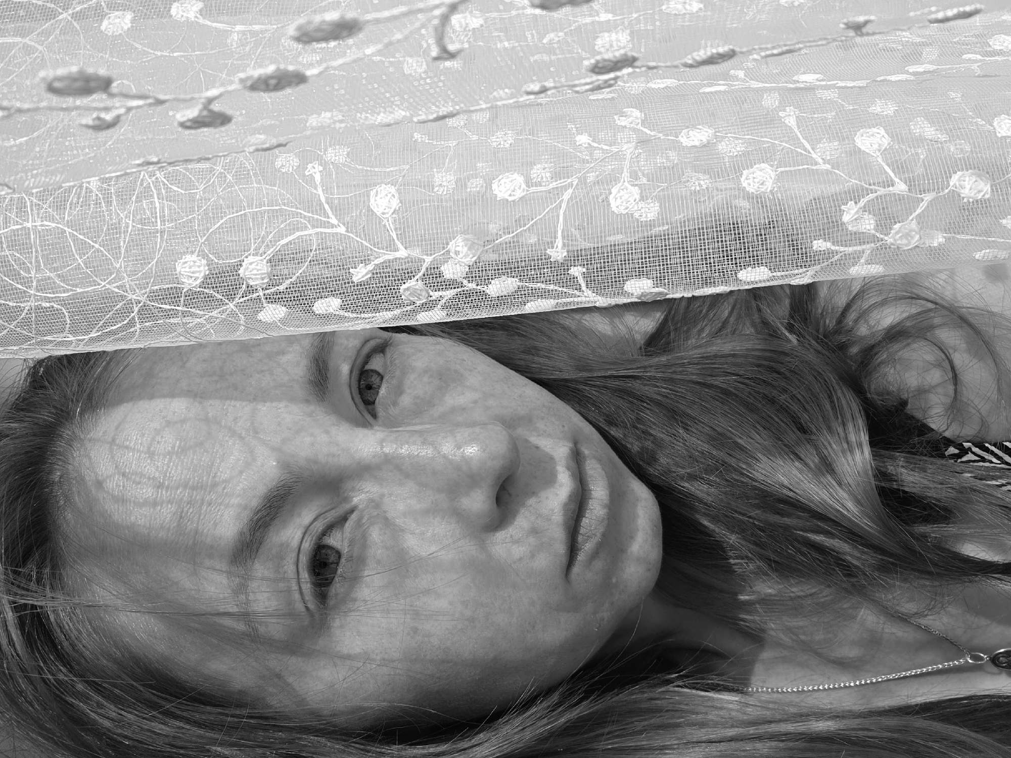 Woman photographed in intimate indoor setting near lace-curtained window