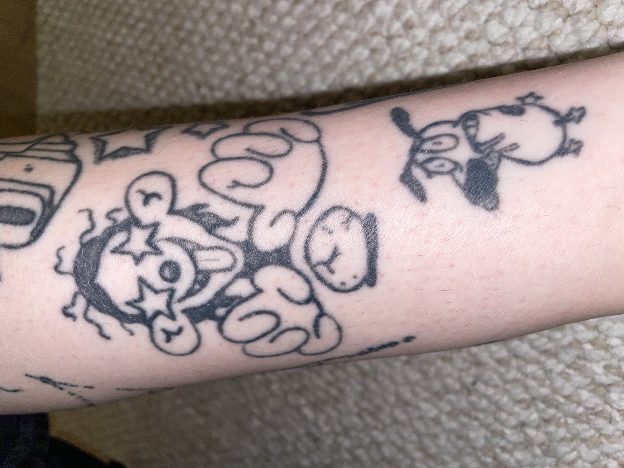 Black ink cartoon tattoos on a forearm, shot from multiple angles