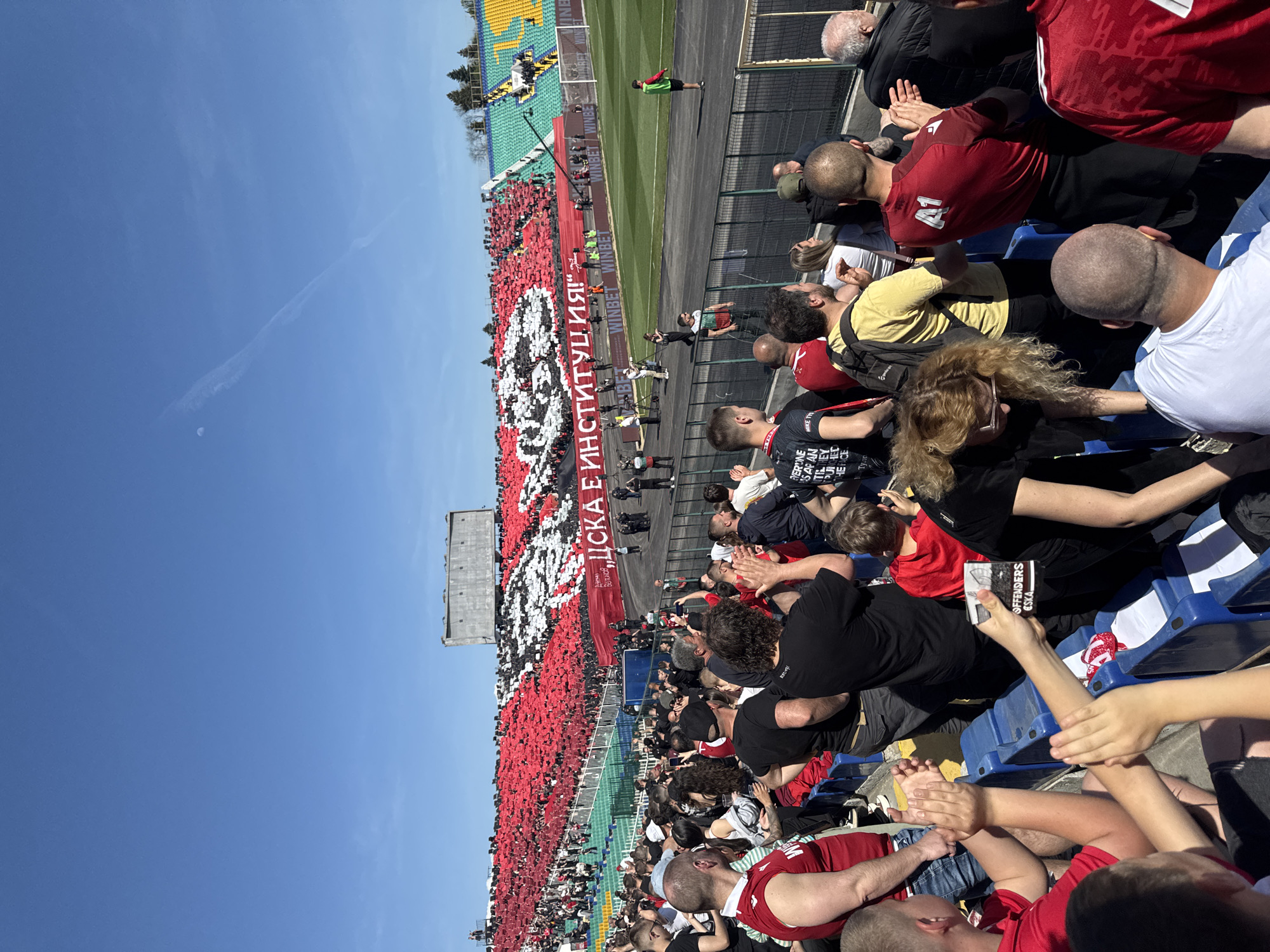 Soccer stadium packed with red-clad fans during daytime match