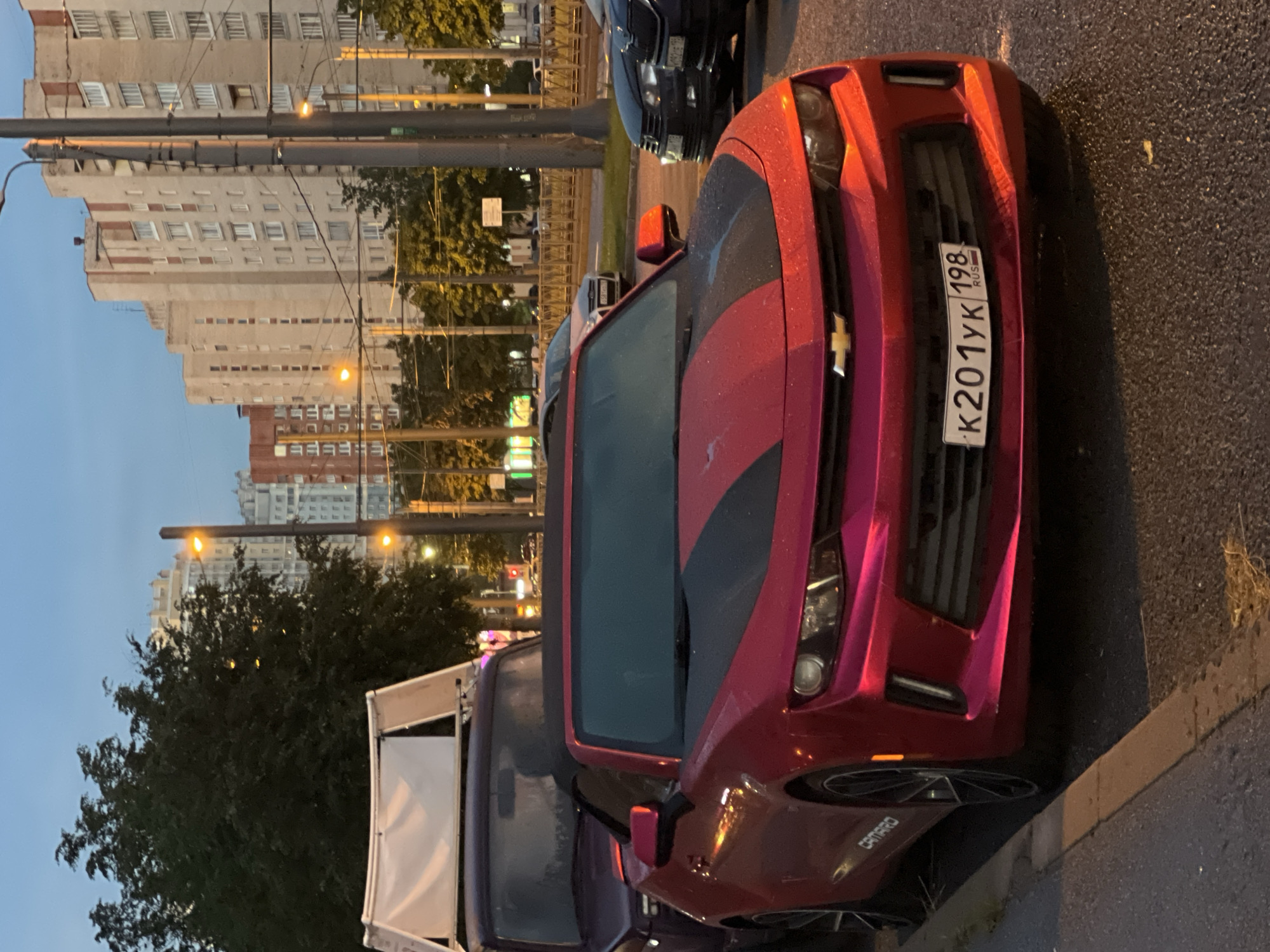 Red Camaro parked on a wet Saint Petersburg street at dusk