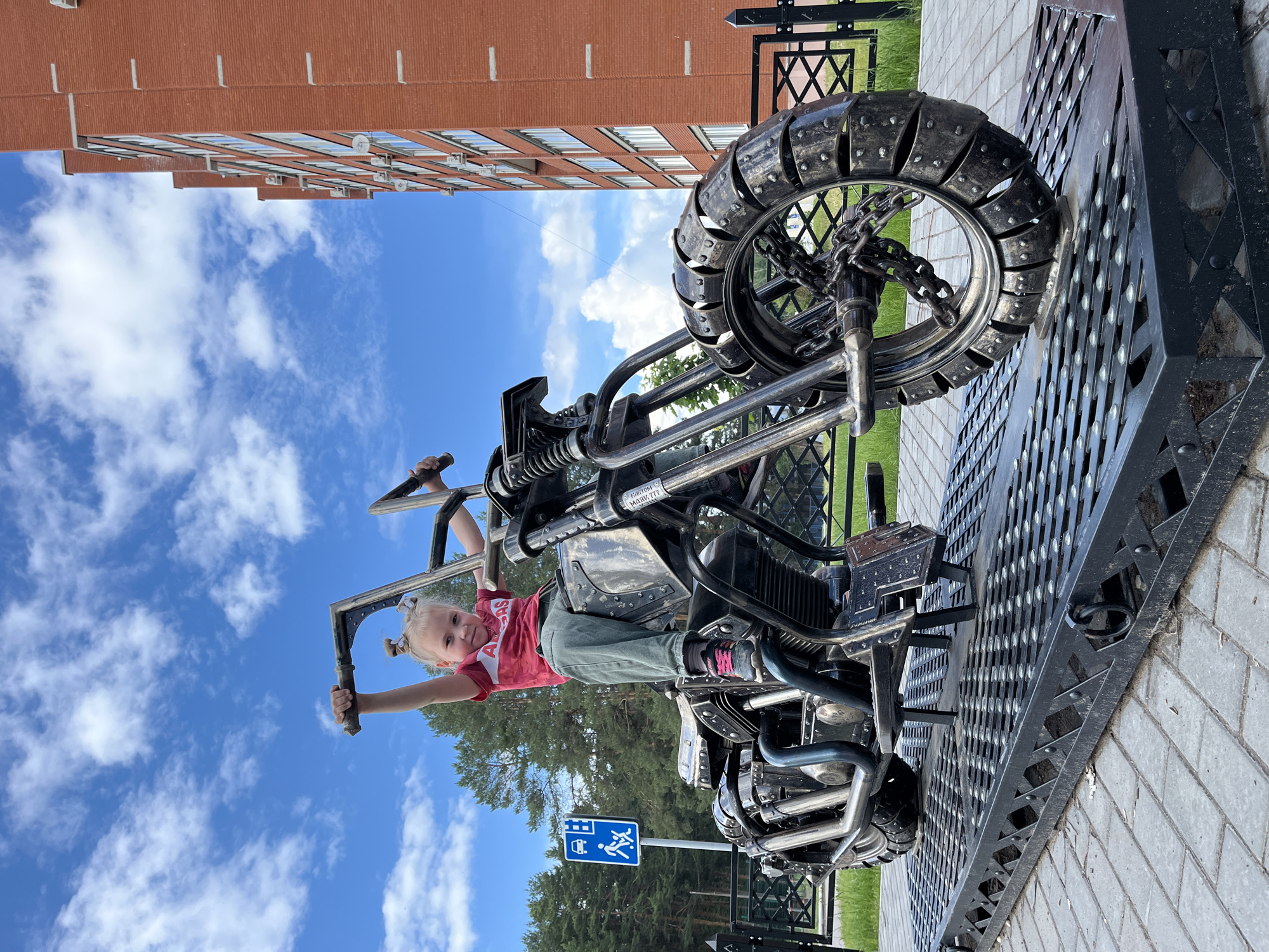 Child plays on metal motorcycle sculpture in Chaikovsky