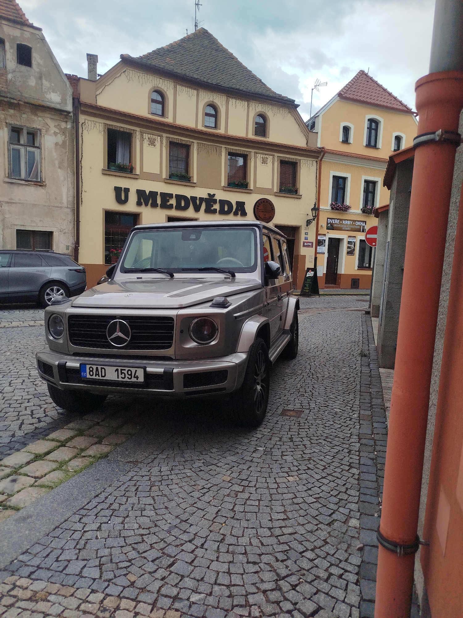 Two cars parked on a cobblestone street in a Czech city.