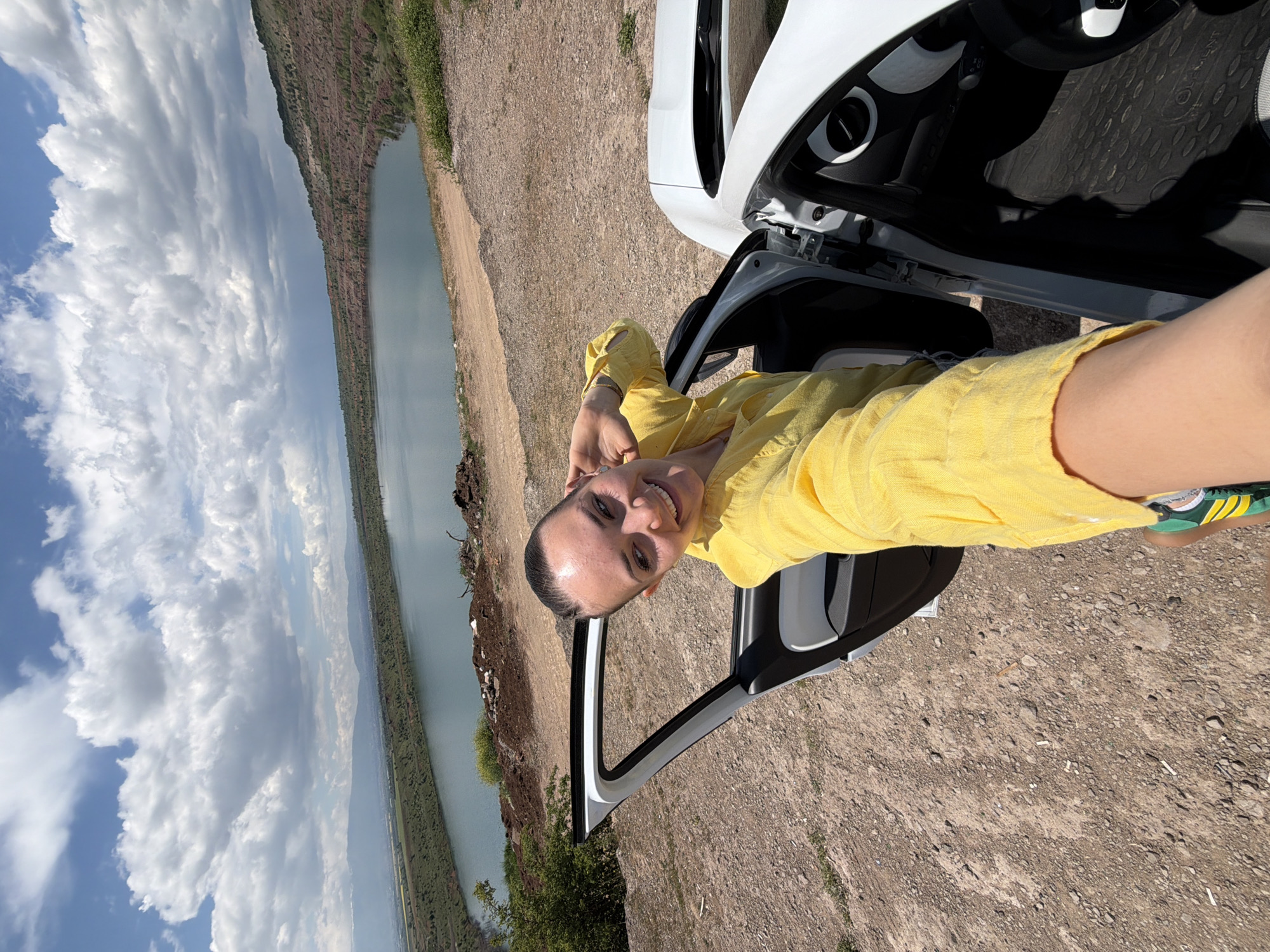 Woman poses by white car at scenic lakeside near Sofia