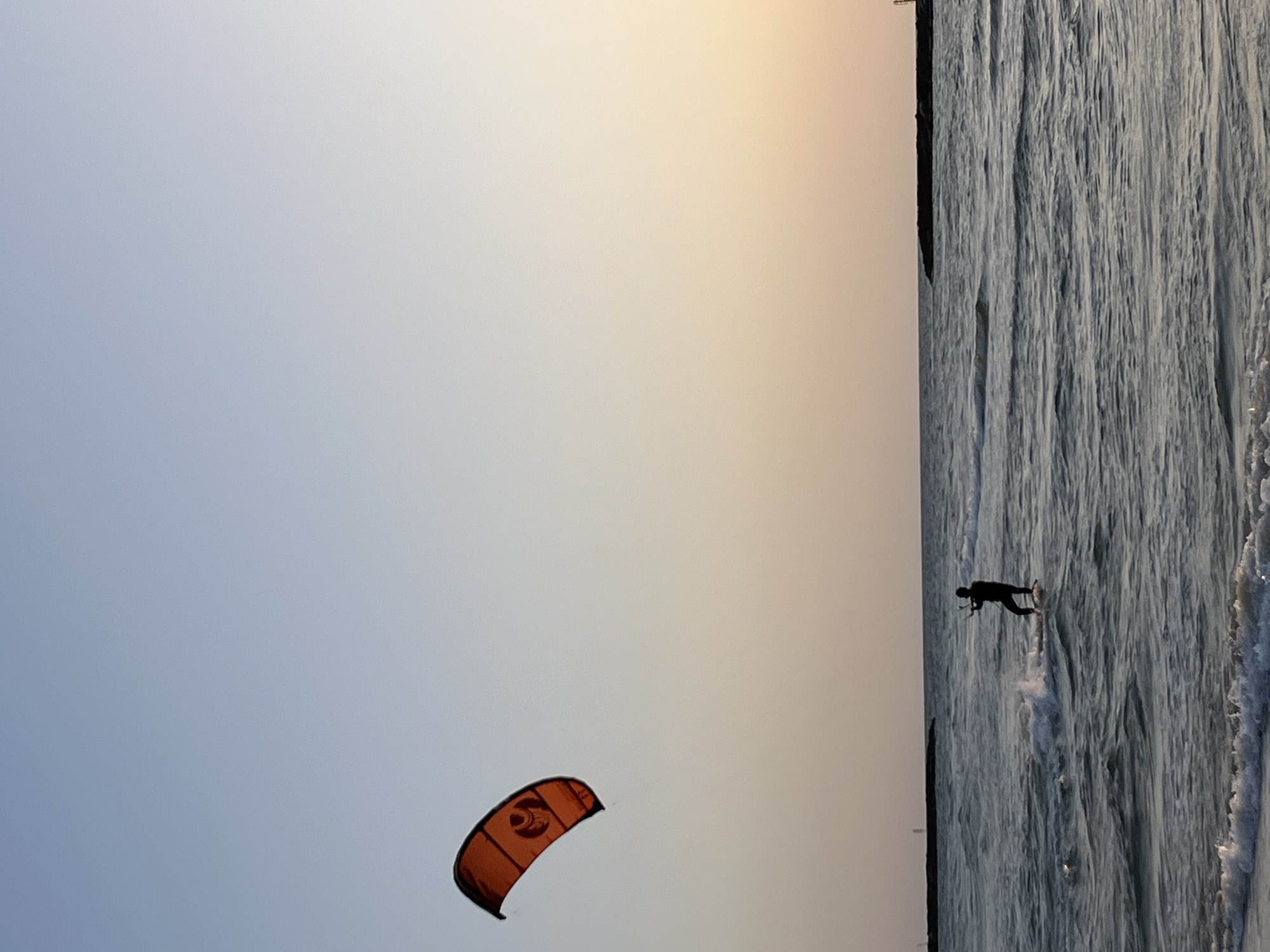 Kitesurfer spotted with orange kite at unidentified coastal location