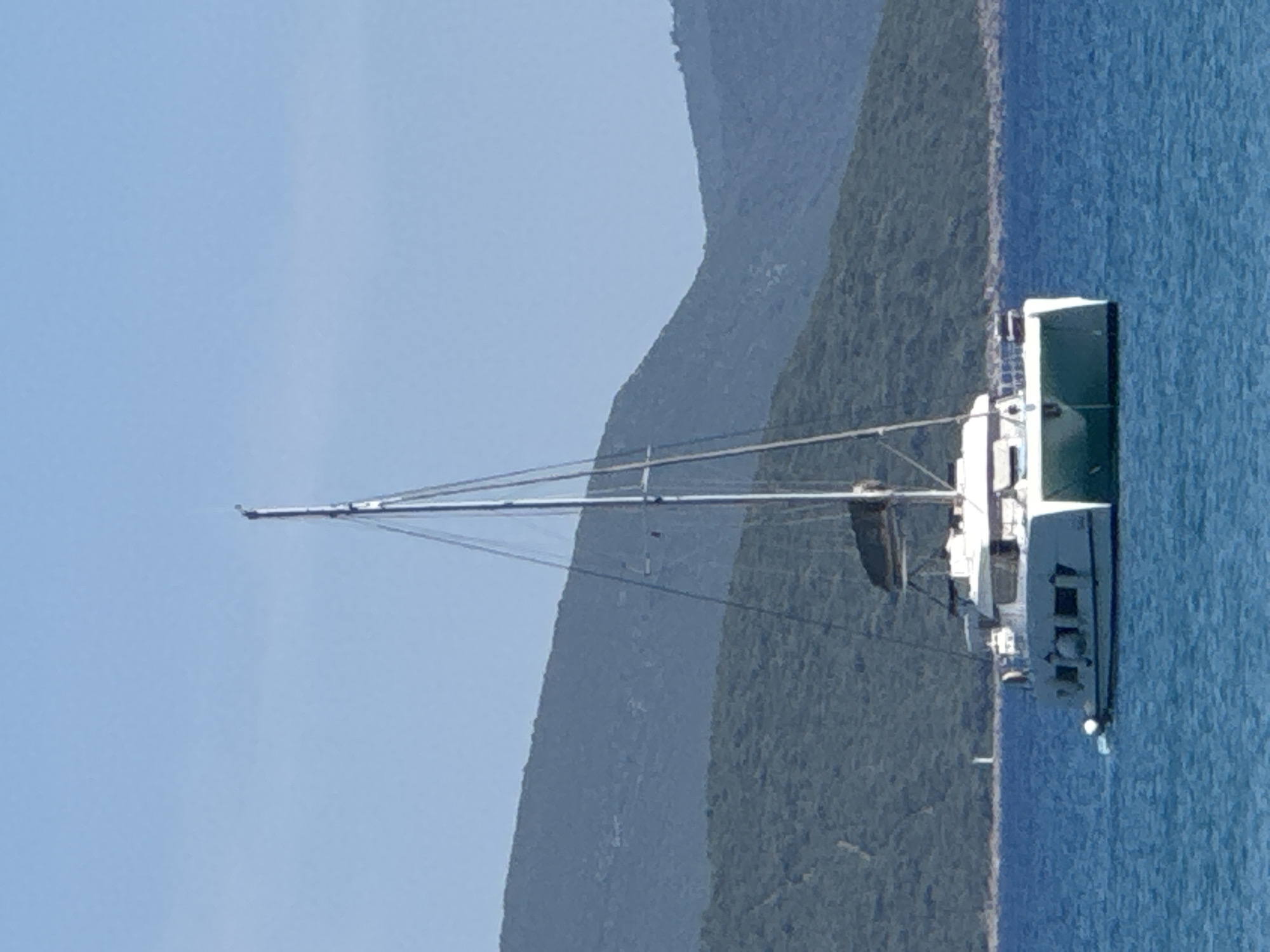 Lazy afternoon on a rocky beach with a catamaran anchored offshore.