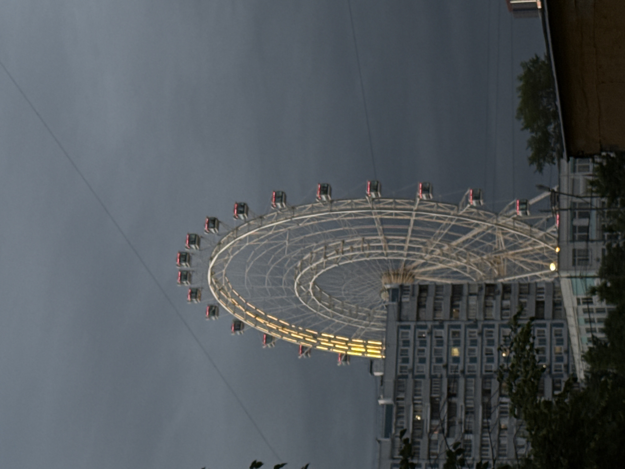 Illuminated Ferris wheel beside apartment building in Dolgoprudny evening