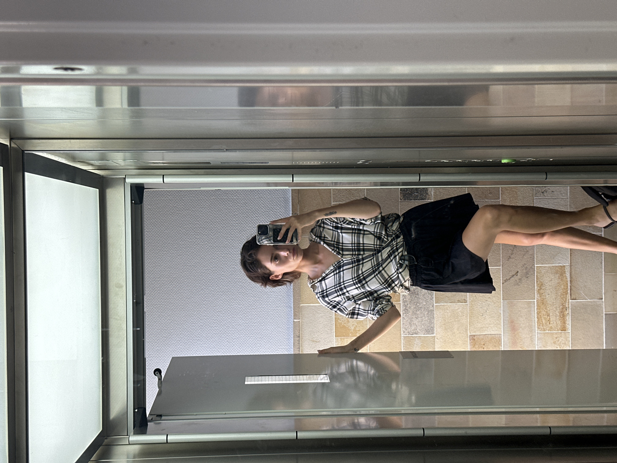 Mirror selfie in a Kiel elevator, checkered shirt and steel walls.