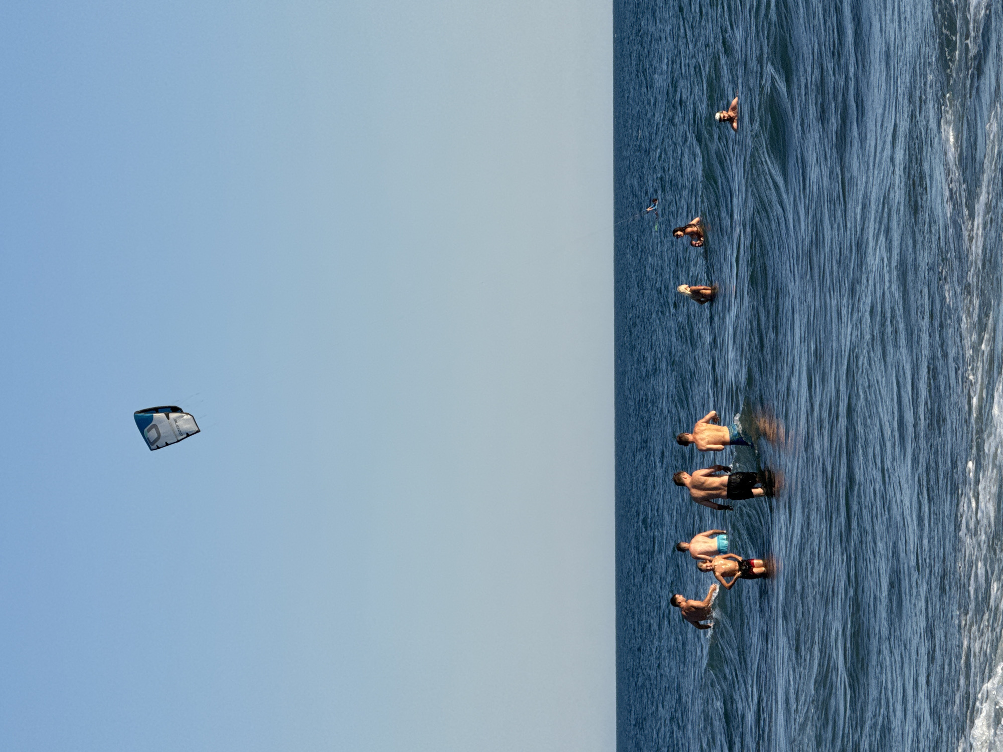 Sunny beach day with kitesurfers offshore and crowds on the sand