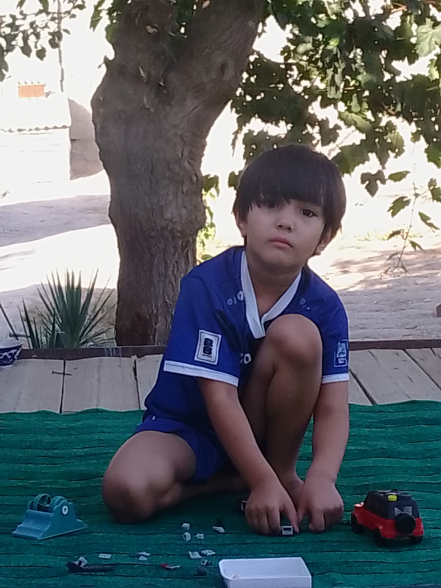 Crouching on a green mat surrounded by small toys outdoors