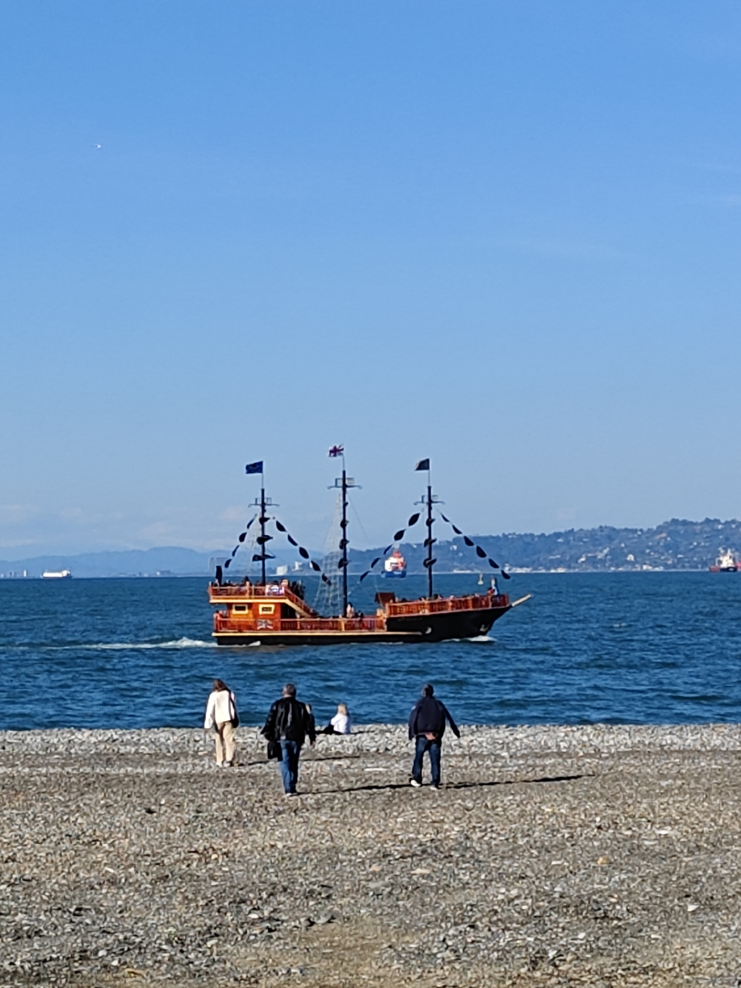 Pirate ship sails past pebble beach as onlookers watch