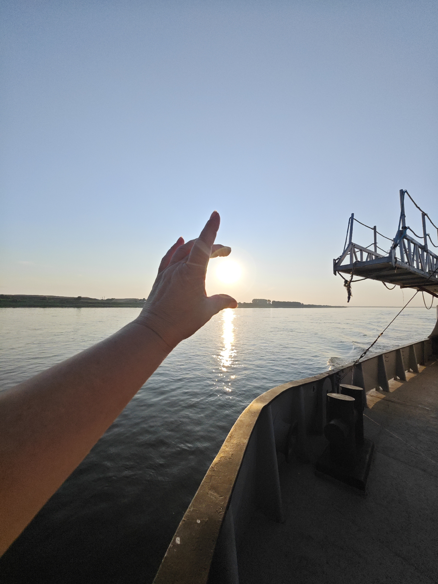 Hand reaching toward a river sunset from a ship deck