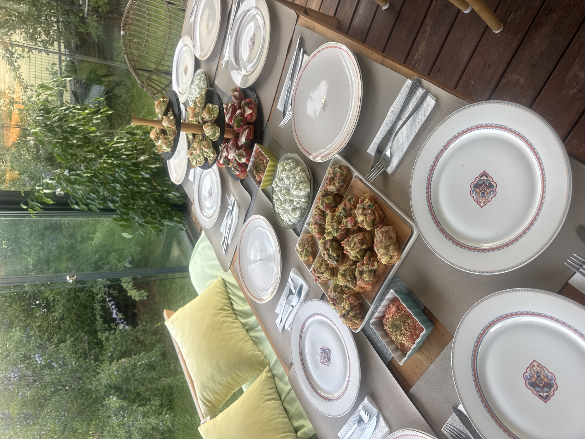 Outdoor deck dining table spread with food, green forest backdrop