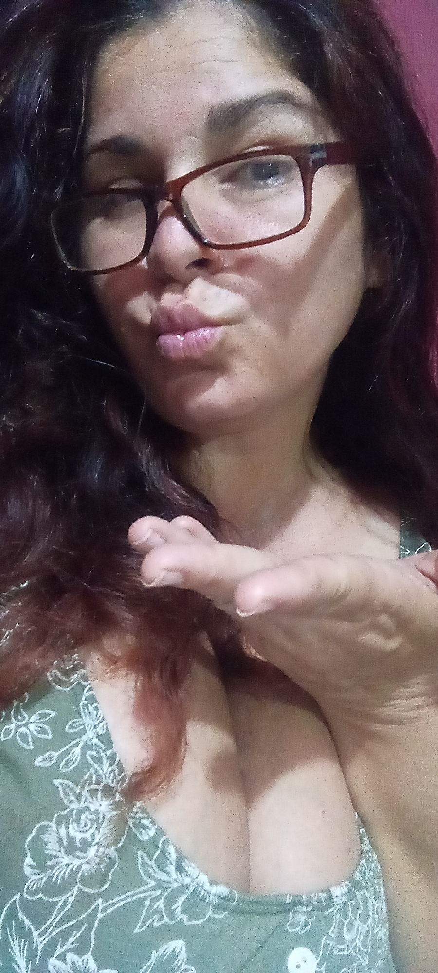 Woman takes playful kiss-blowing selfie in green floral top