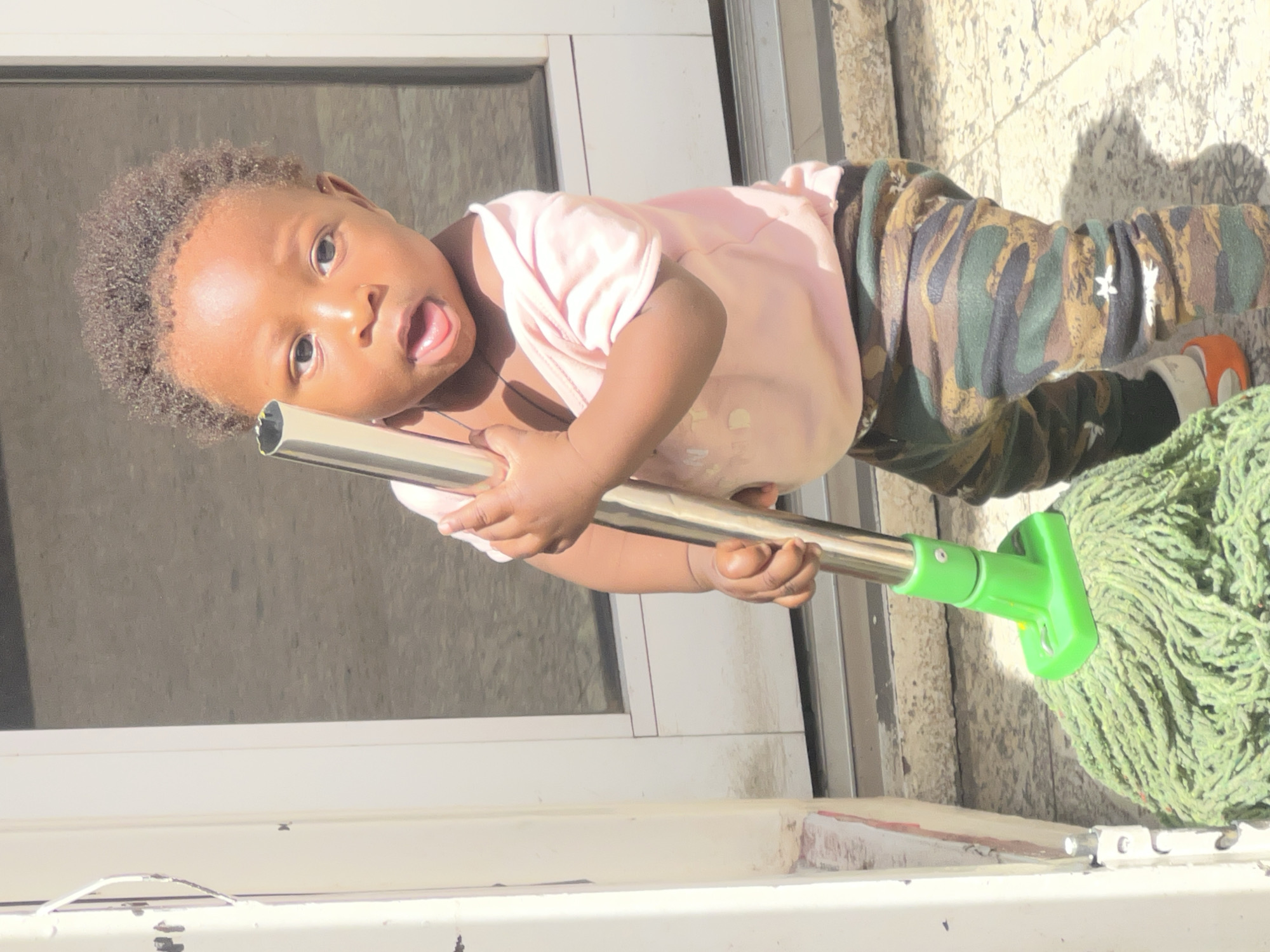 Toddler plays with mop, poses playfully in Gura Top