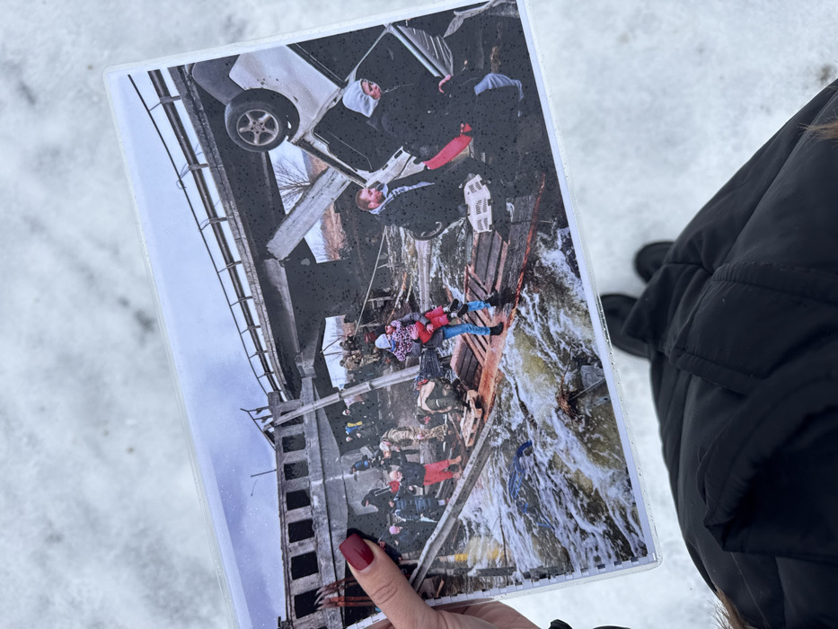 Person holds bridge destruction photo in snowy Irpin Ukraine