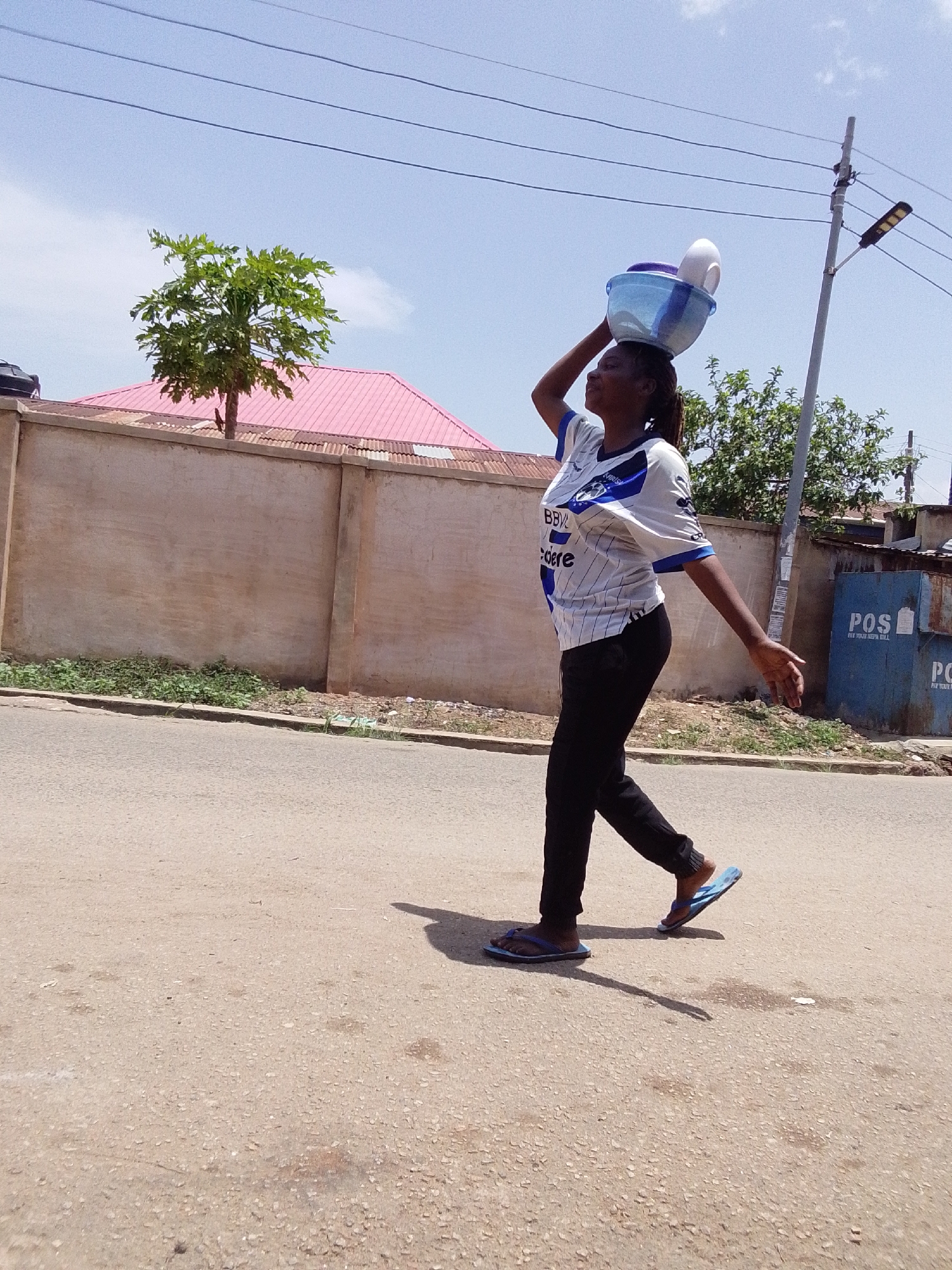 Pedestrians carry goods, push wheelbarrows on neighborhood streets