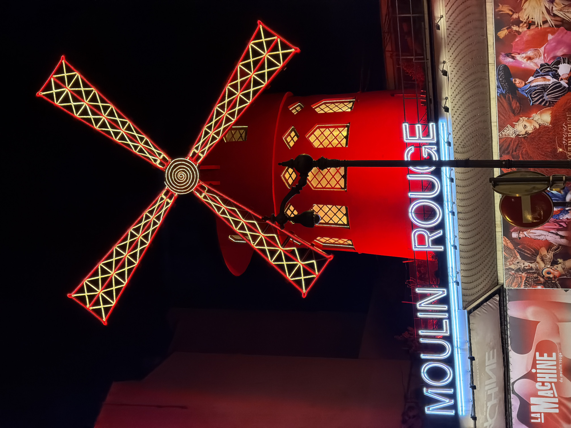 Evening street life documented around illuminated Moulin Rouge, Paris