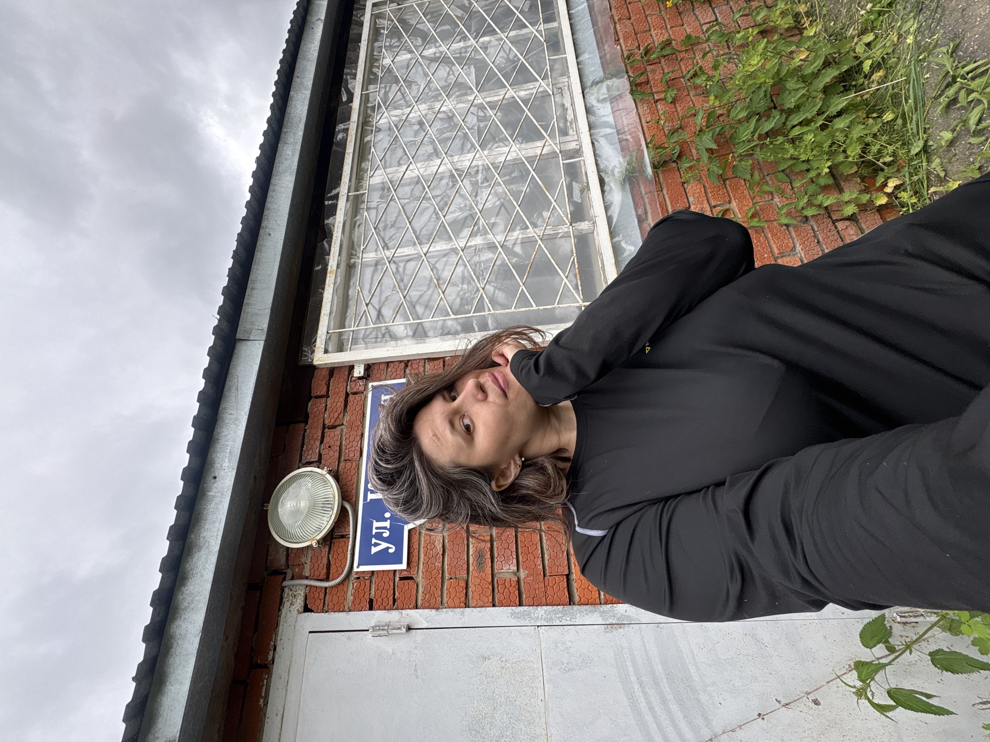 Woman takes playful selfies with plants near brick building