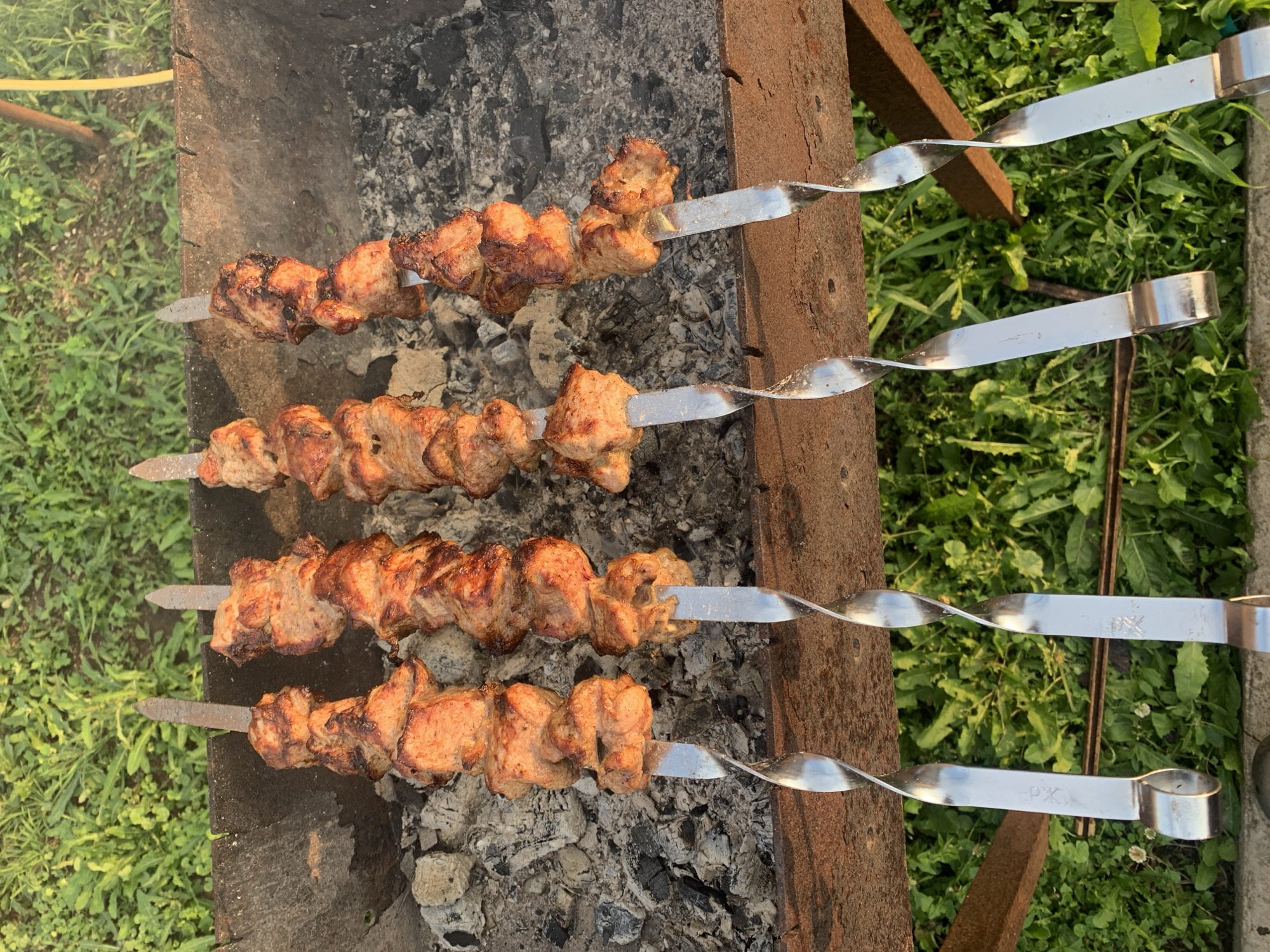 Cubed meat on spiral skewers over a barbecue grill.