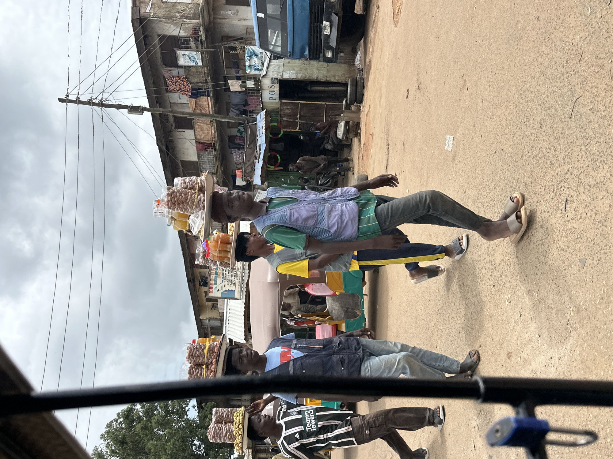 Street vendors and foot traffic on a dusty Jos road