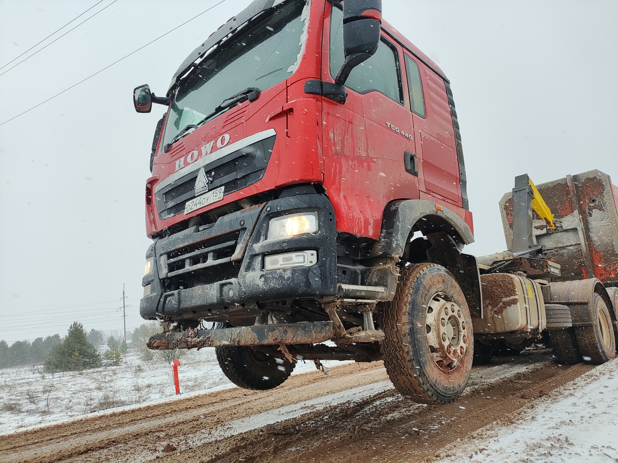 Red semi-truck travels snow-covered muddy road amid falling snow