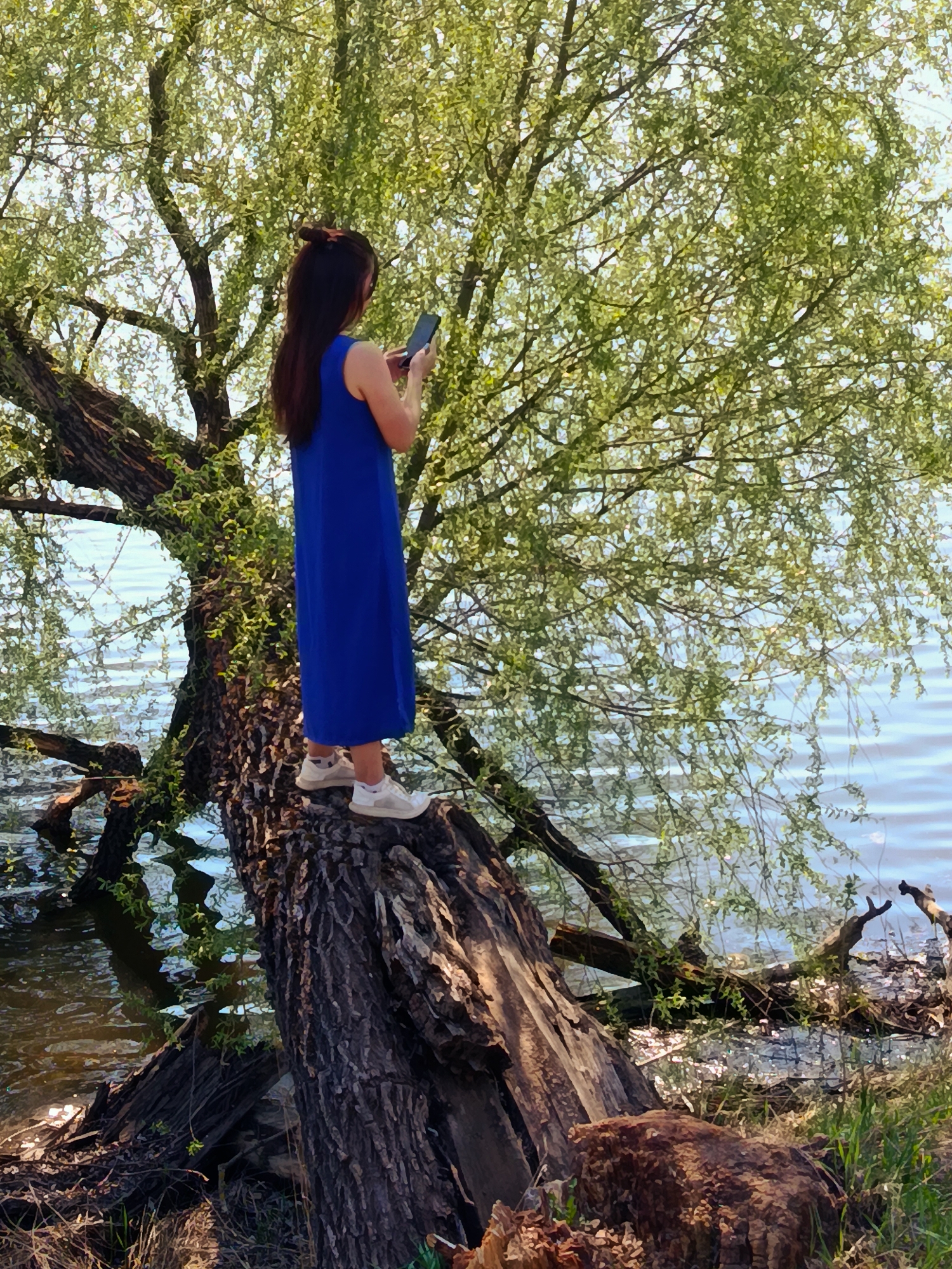 Woman poses on fallen tree with phone near water