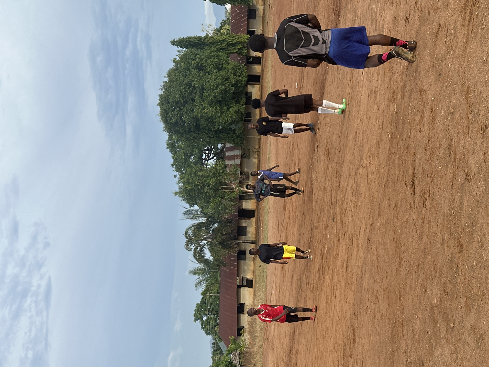 Seven young men gather outdoors on dirt surface