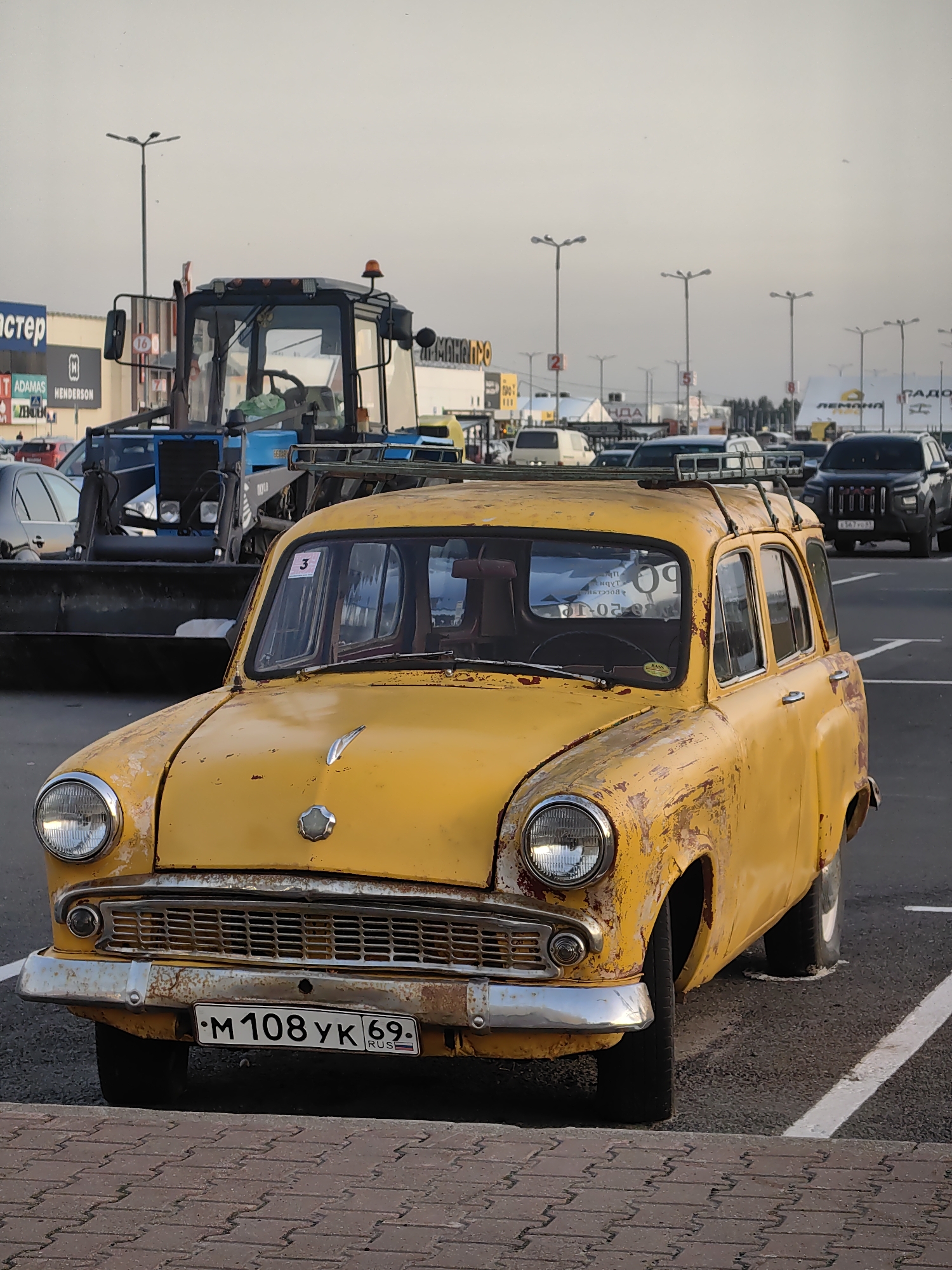 Rusty vintage yellow station wagon parked in Tver shopping lot