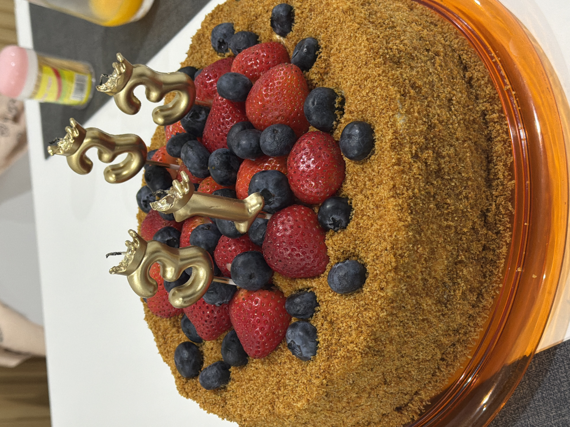 Third birthday cake with berry toppings and gold candles, Kathu