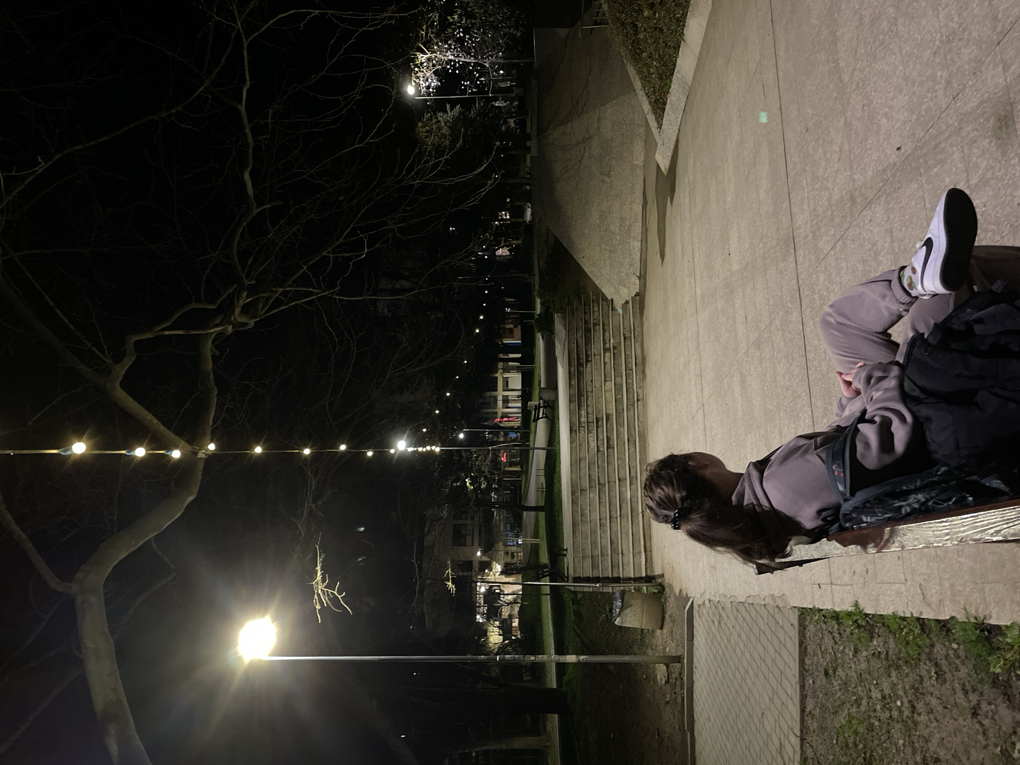 Woman sits in illuminated park during evening in Veliko Tarnovo