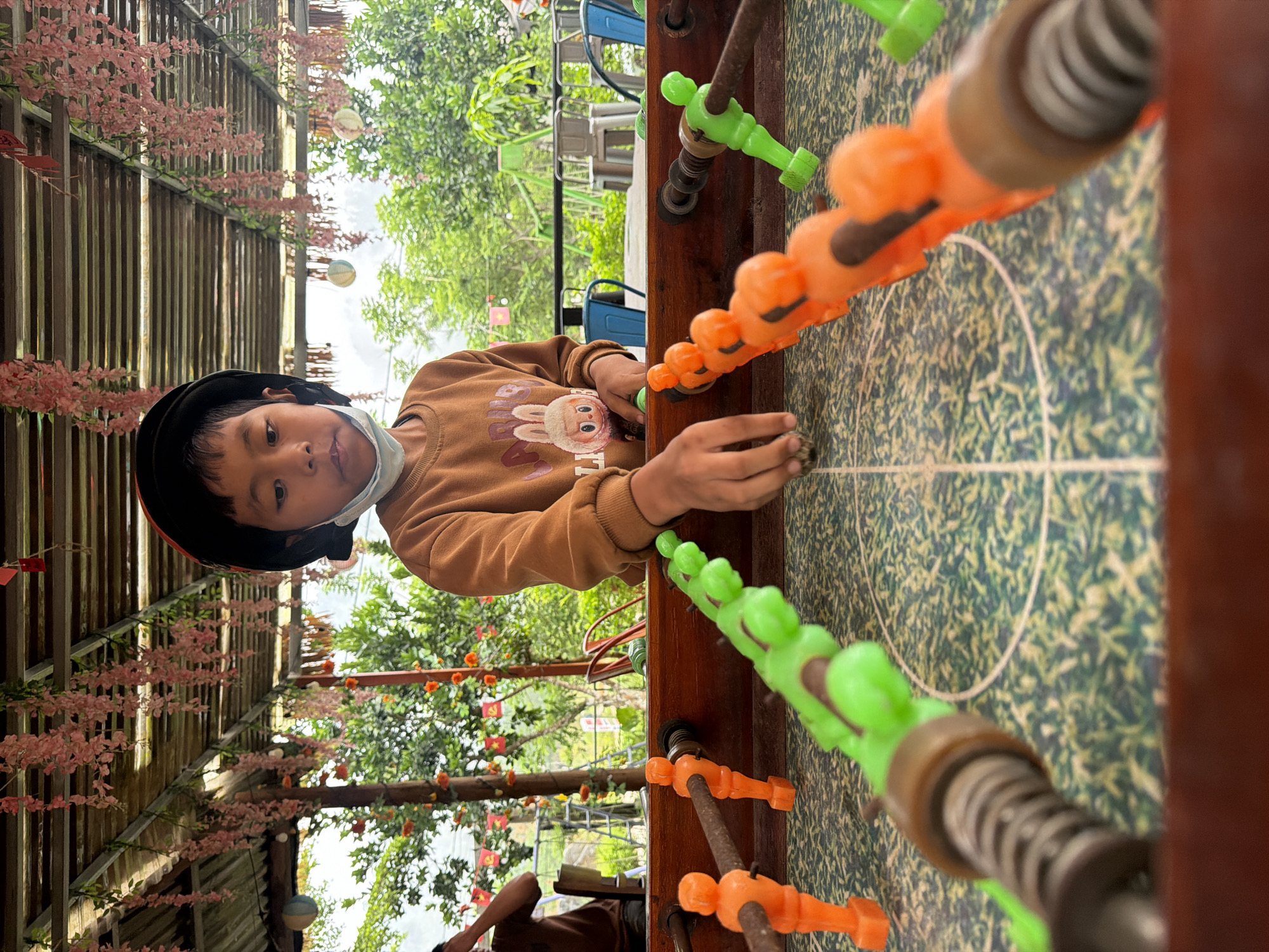 Masked child plays foosball at late-night Đà Nẵng cafe