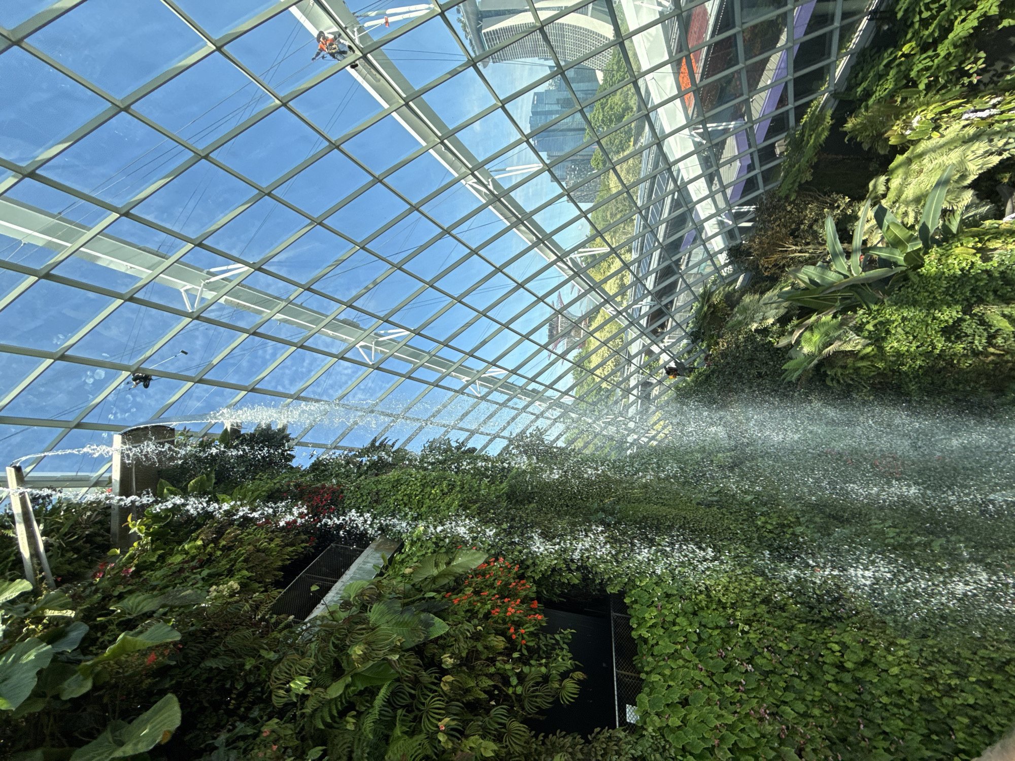 Visitors explore glass conservatory featuring waterfalls, dinosaurs, botanical displays