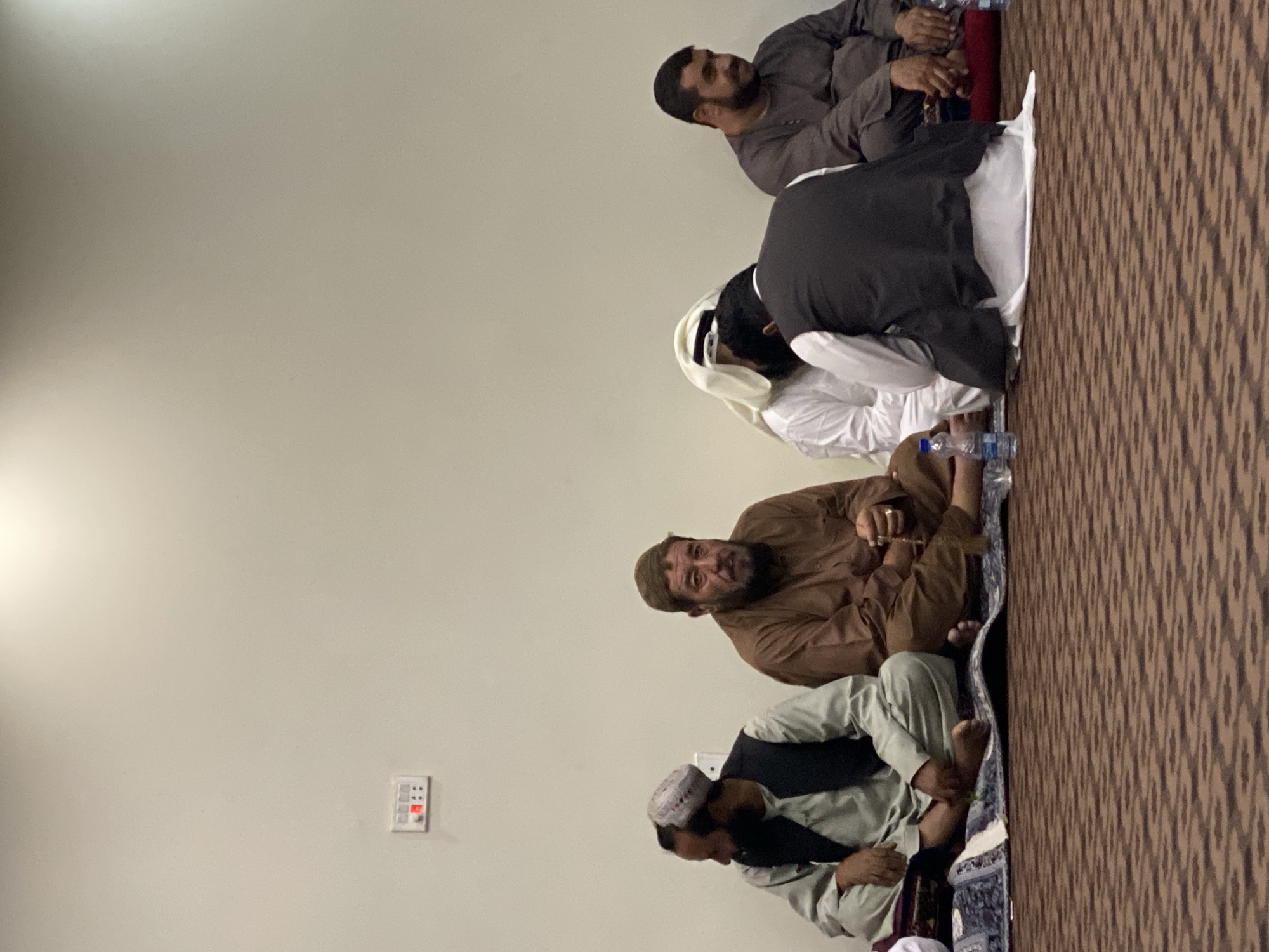 Five people seated on carpet inside a Kandahar interior space