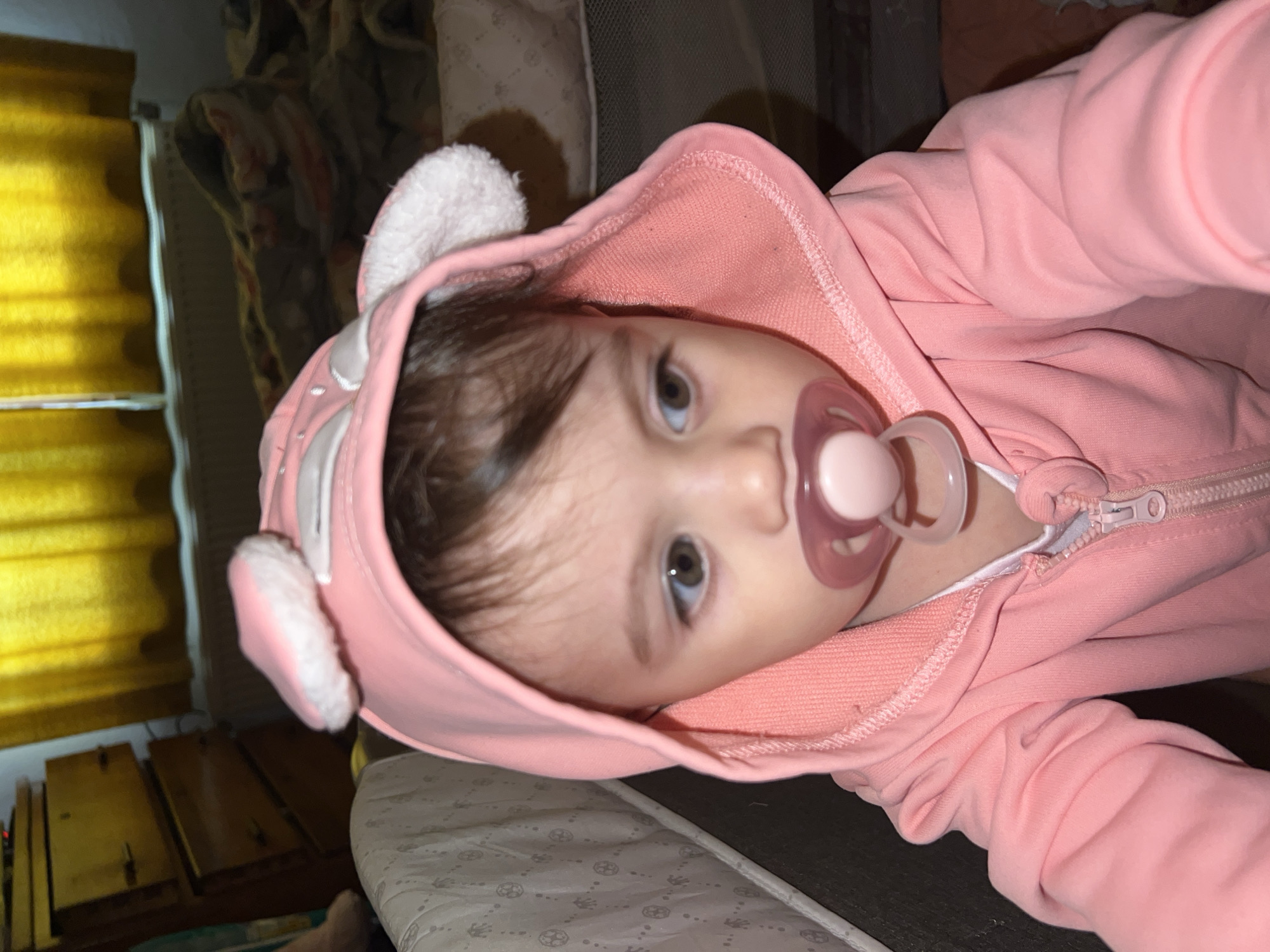 Baby in pink hooded outfit rests peacefully in Elena crib