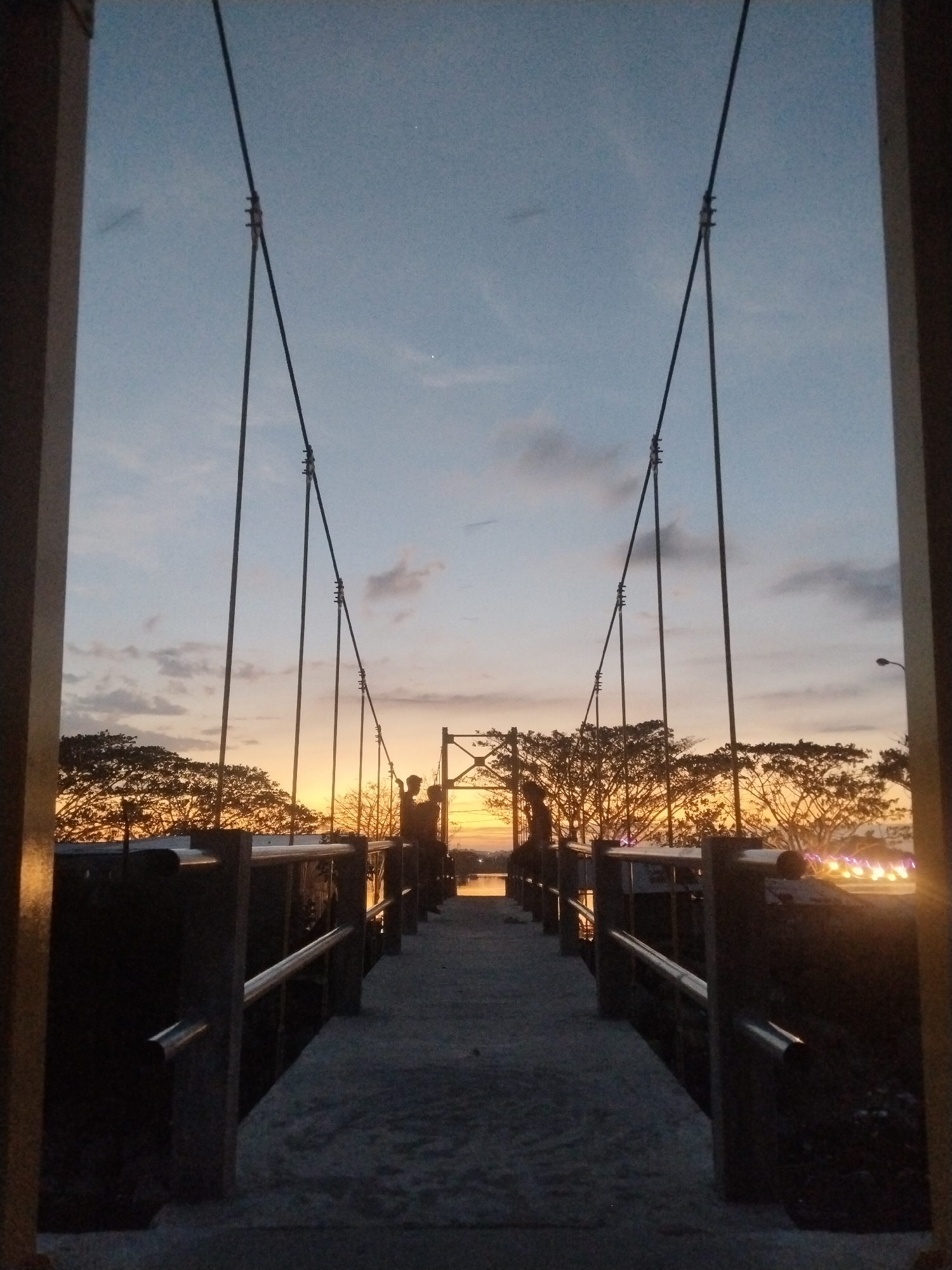 Pedestrians gather on Lhokseumawe suspension bridge at twilight