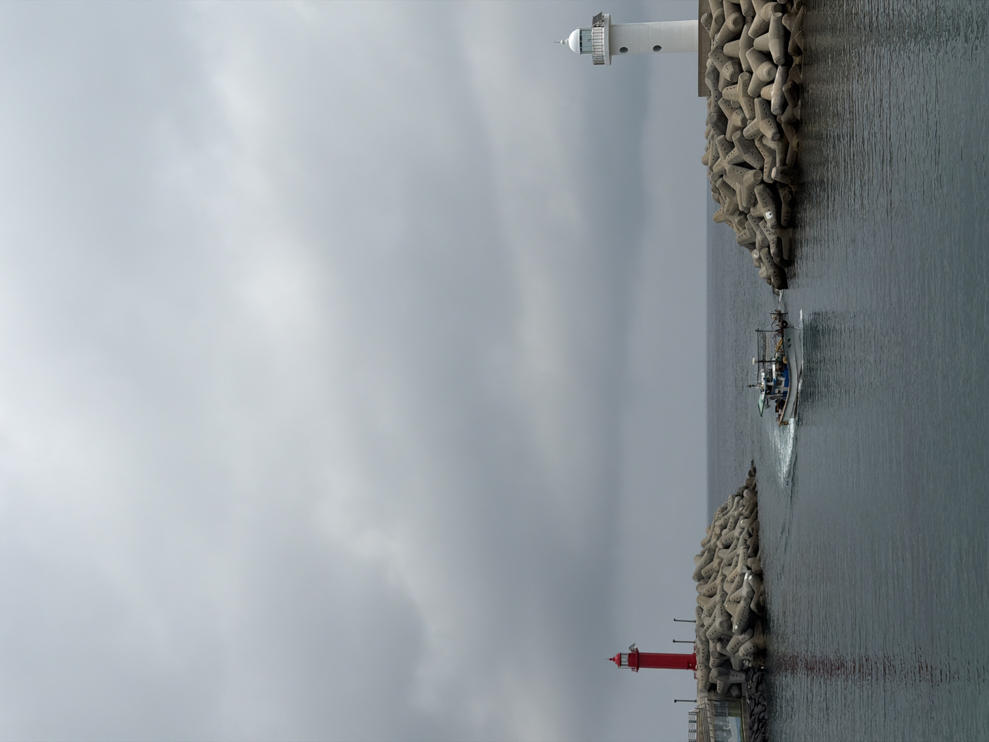 Fishing boat passes through twin-lighthouse harbor entrance in Jeju