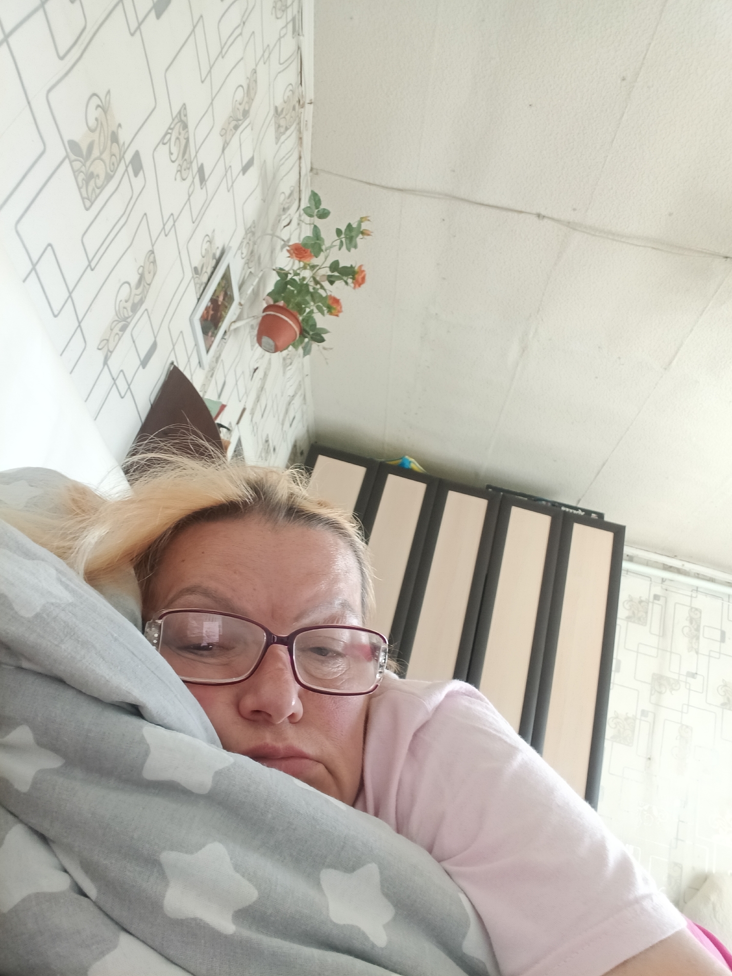 Woman rests in bed with star-patterned pillow, plant visible