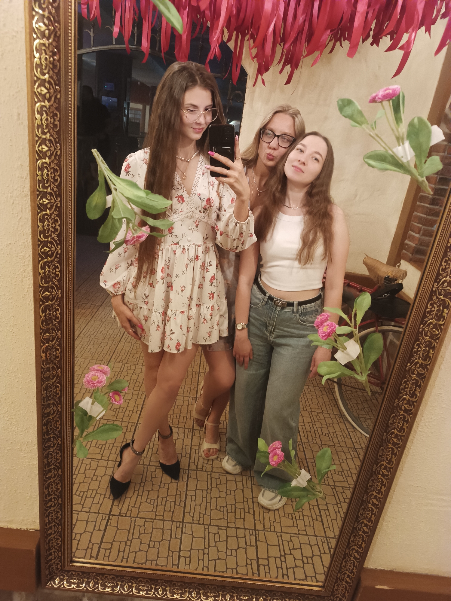 Women take mirror selfies at indoor venue Friday evening