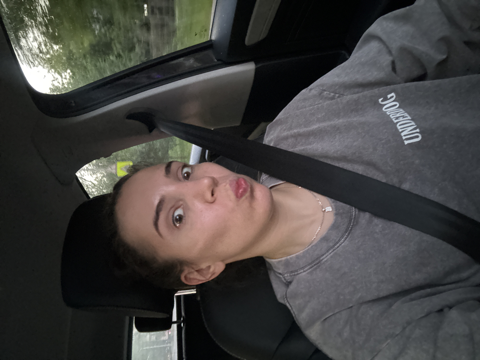 Driver's seat selfie in Moscow, 'UNDERDOG' sweatshirt, seatbelt on