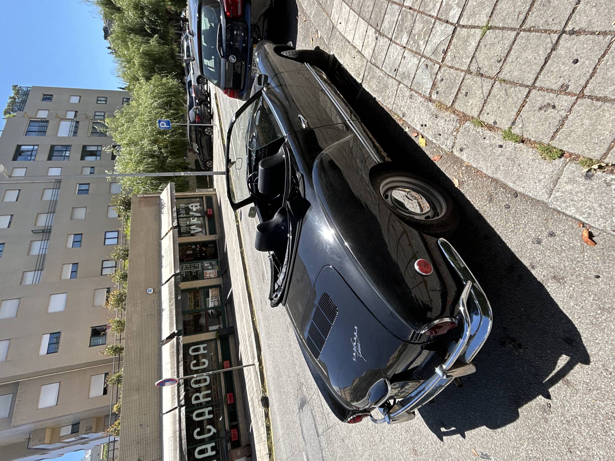 Black Karmann Ghia convertible parked on a city street, top down.