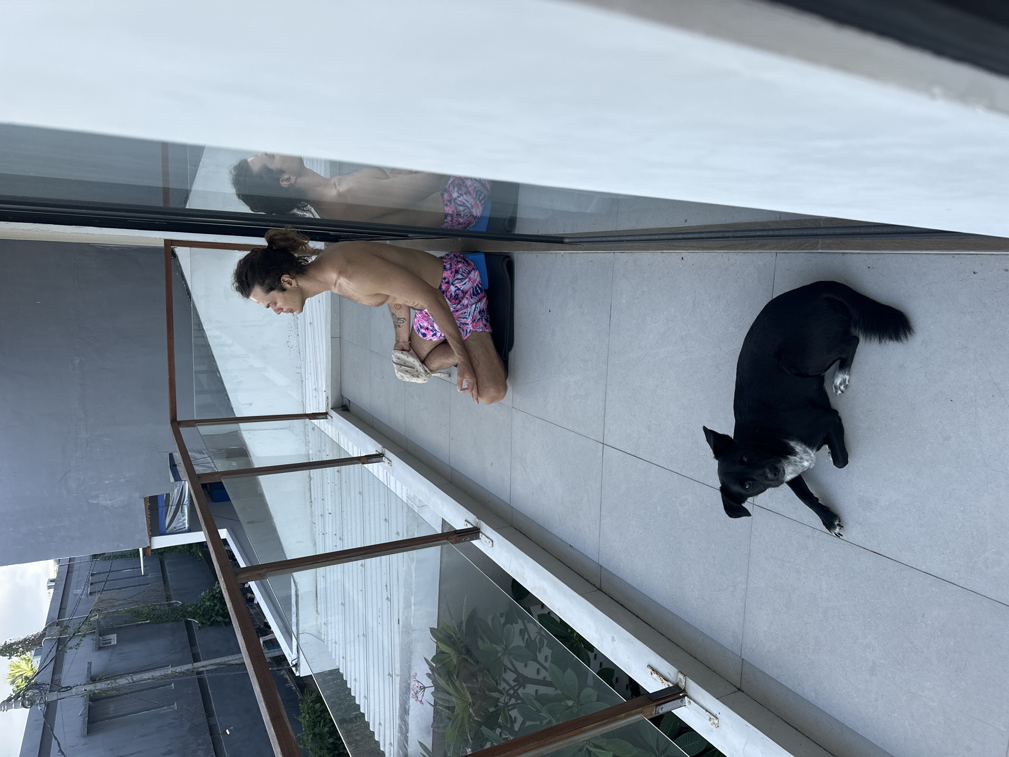 Man meditates on balcony with dog in Mengwi