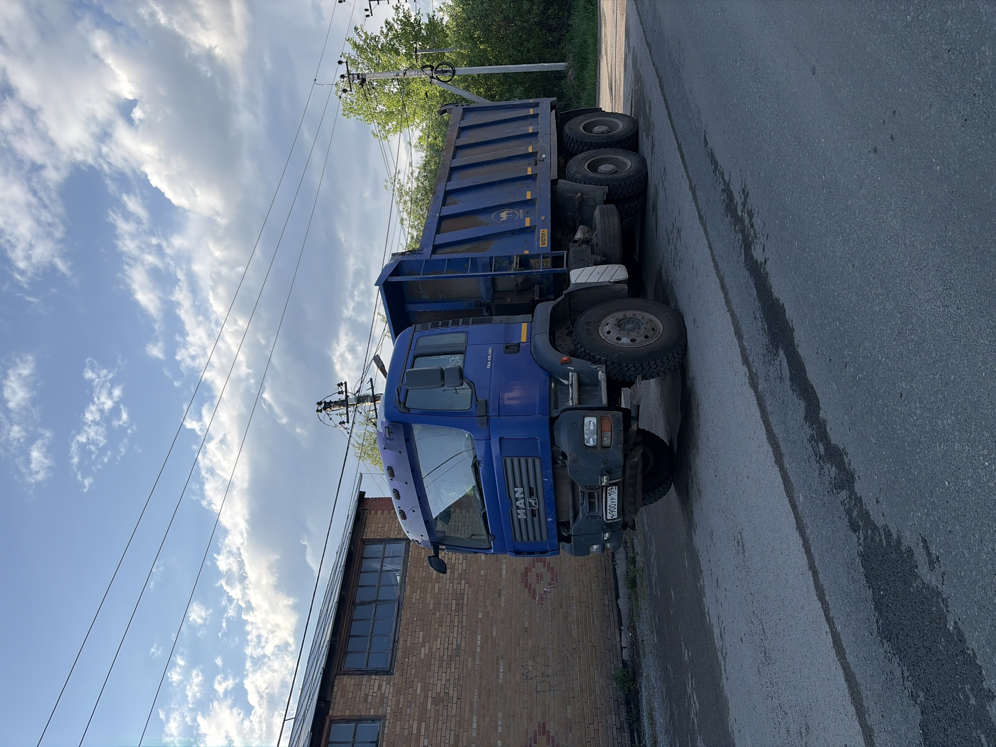 Dump truck parked, traffic flows on Perm residential street