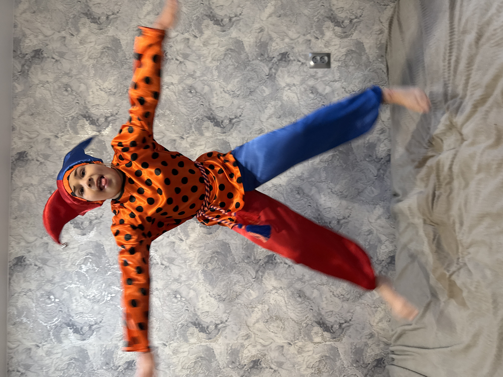 Child plays in jester costume, jumps on bed