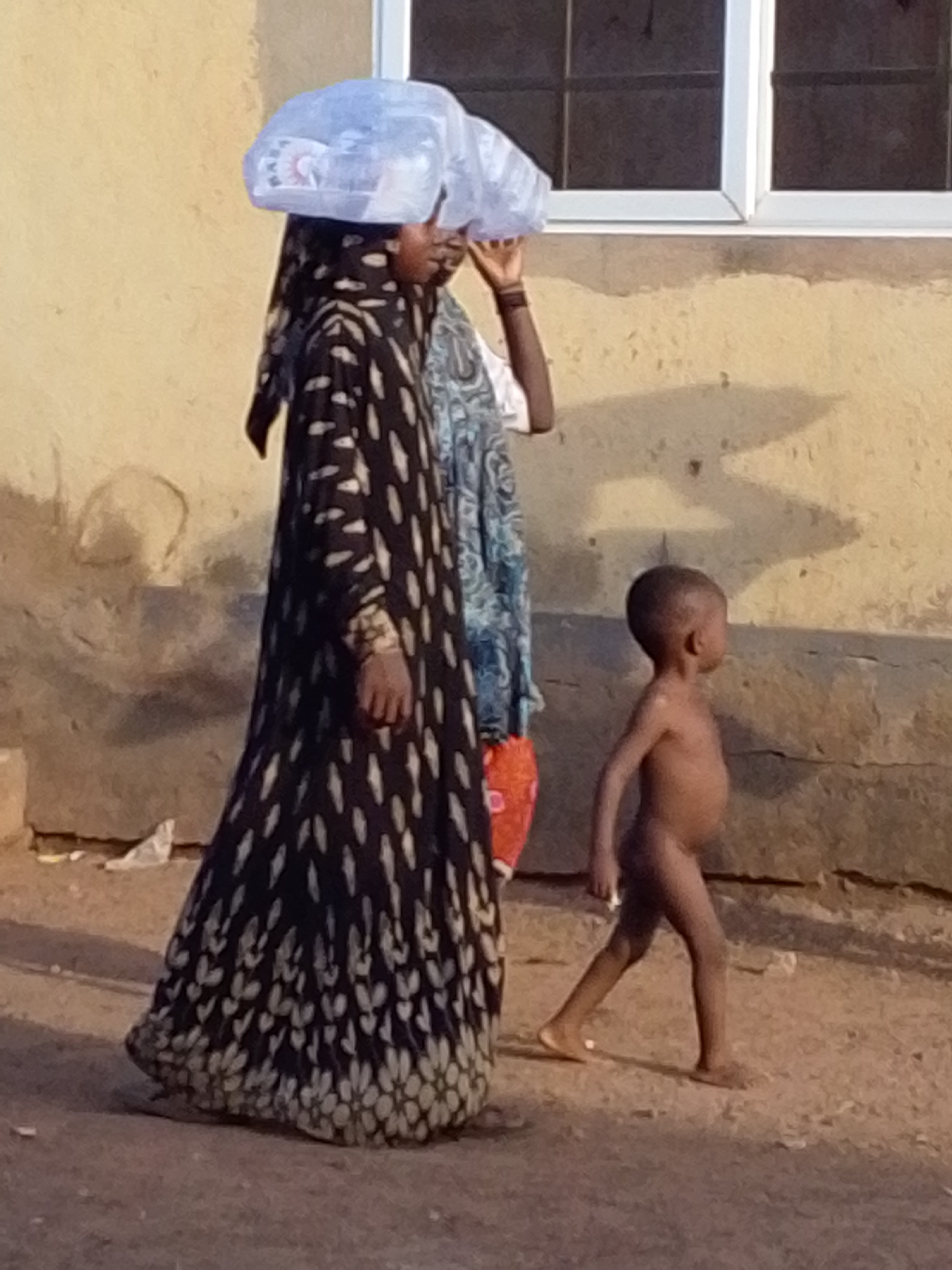 Child and woman walk dirt road in Tamale