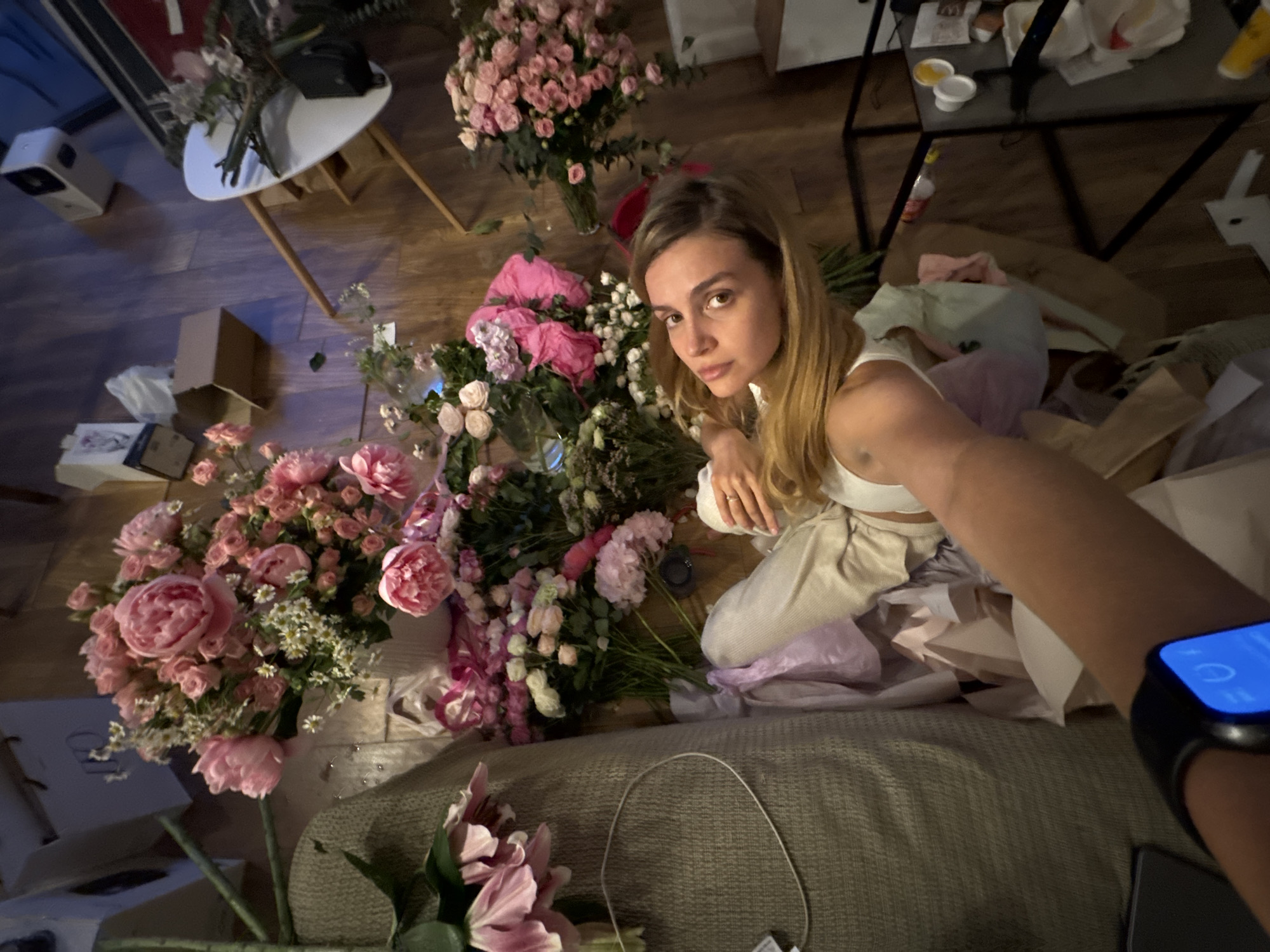 Woman prepares flower arrangements on floor with scattered blooms