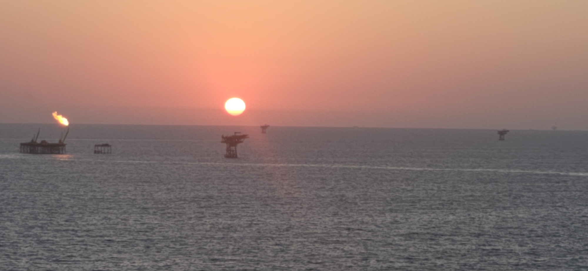 Offshore oil rig at sunset with flare burning